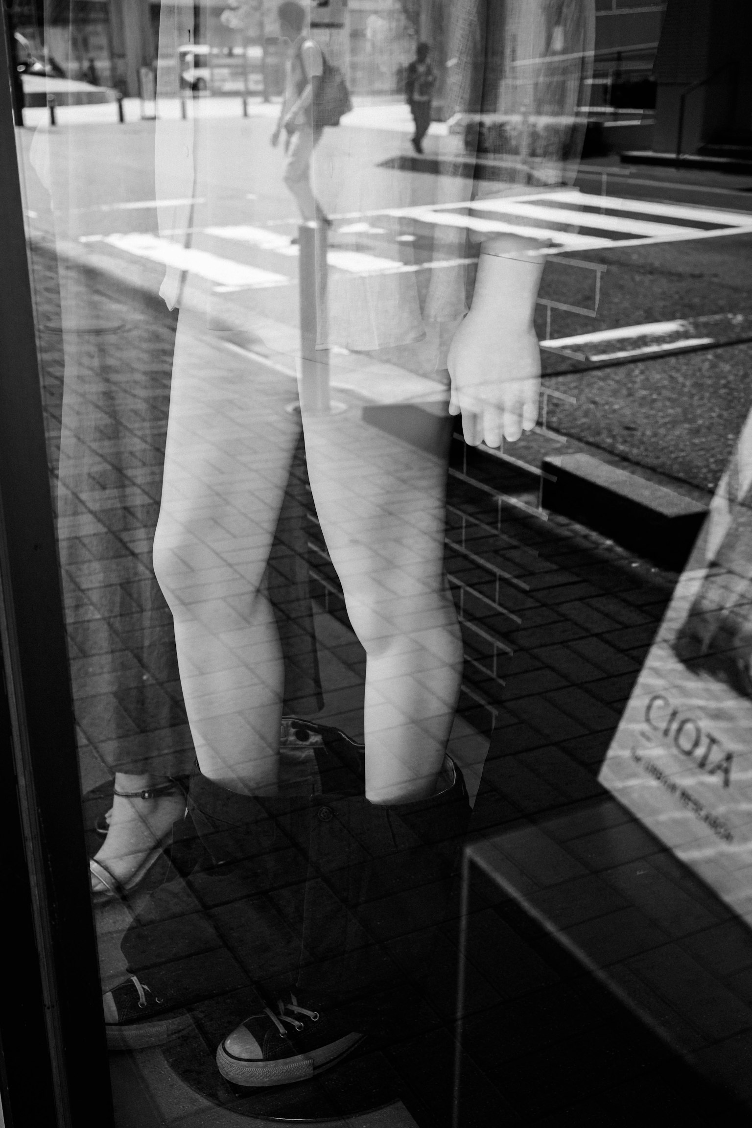 Foto hitam putih yang menunjukkan kaki dan sepatu yang terpantul di jendela