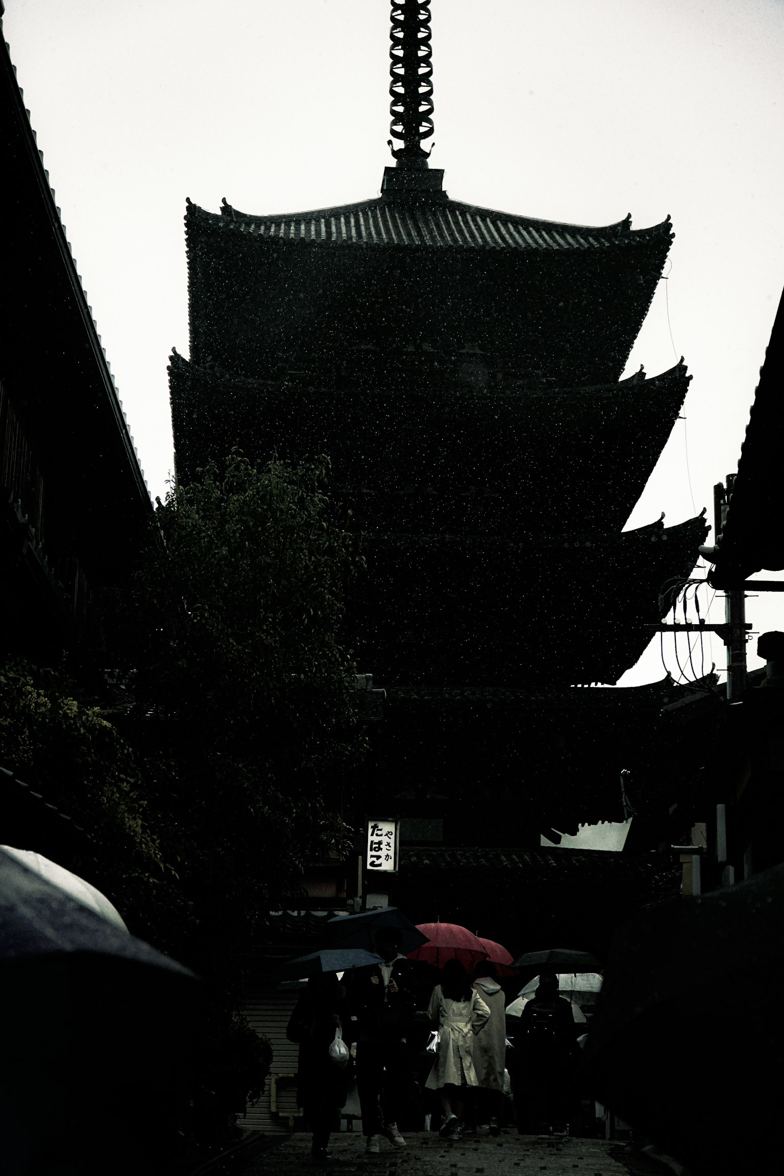 Five-story pagoda silhouetted against a rainy sky with people holding umbrellas