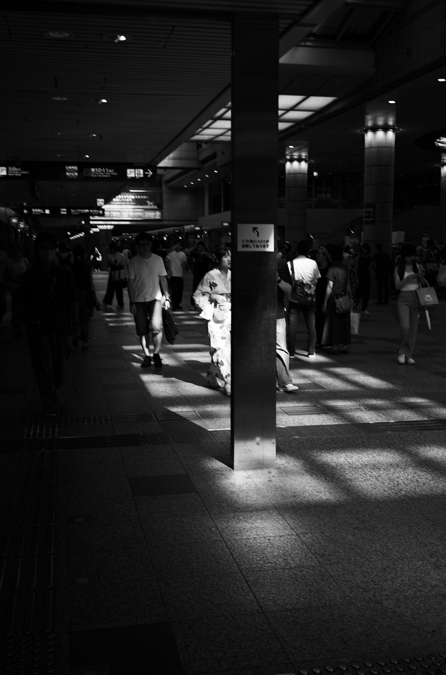 Foto in bianco e nero di un interno di stazione affollato con persone e contrasti di luce e ombra