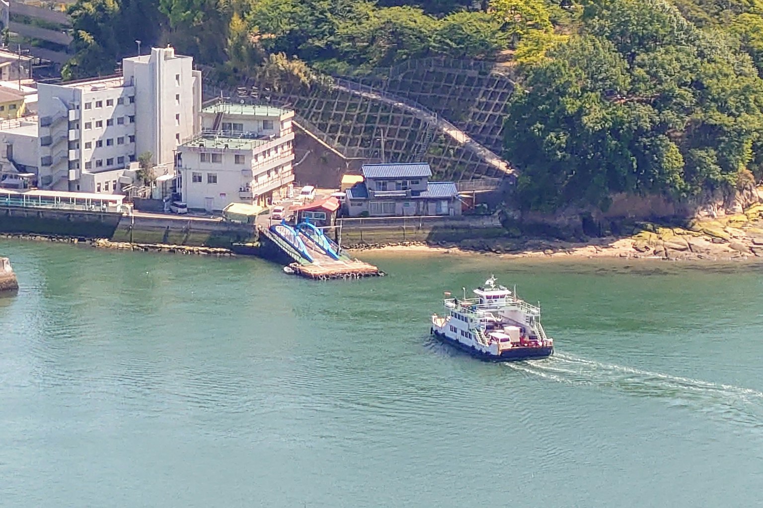 Un ferry navegando en aguas tranquilas cerca de un muelle y edificios en la costa