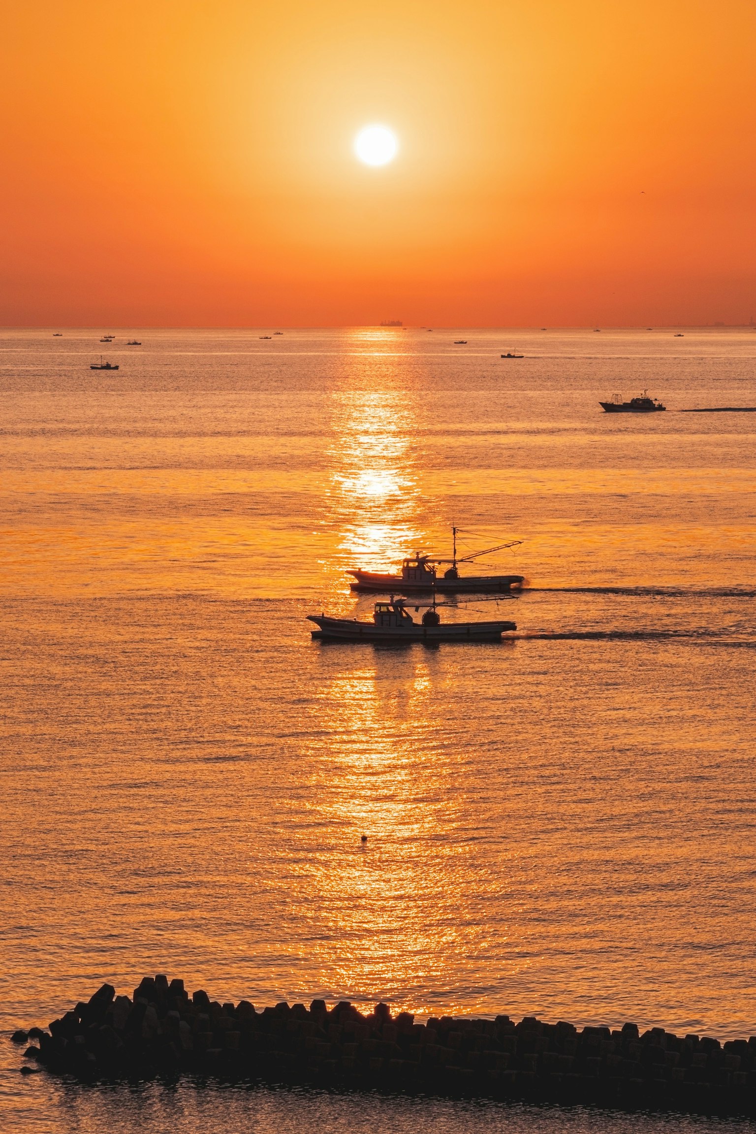 Hermoso paisaje con un atardecer naranja reflejándose en el mar y pequeños barcos