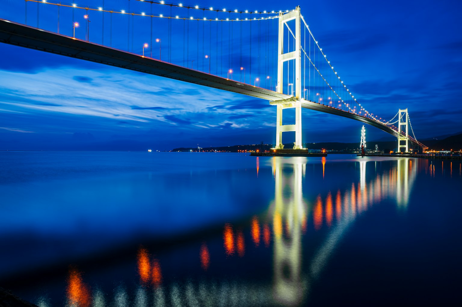 Vista bellissima di un ponte illuminato sotto un cielo notturno blu con riflessi sull'acqua