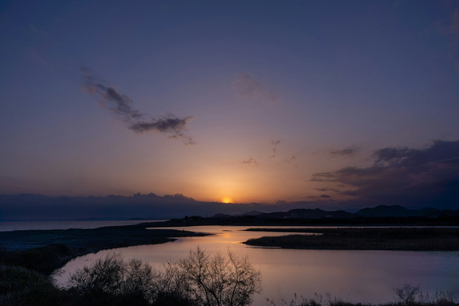 Scenic view of a sunset over a calm river with silhouettes of hills