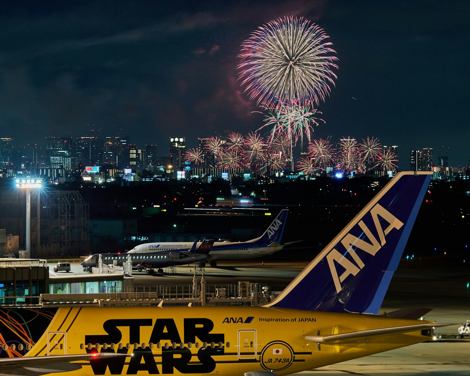 Avion ANA avec un design Star Wars au premier plan et des feux d'artifice dans le ciel nocturne