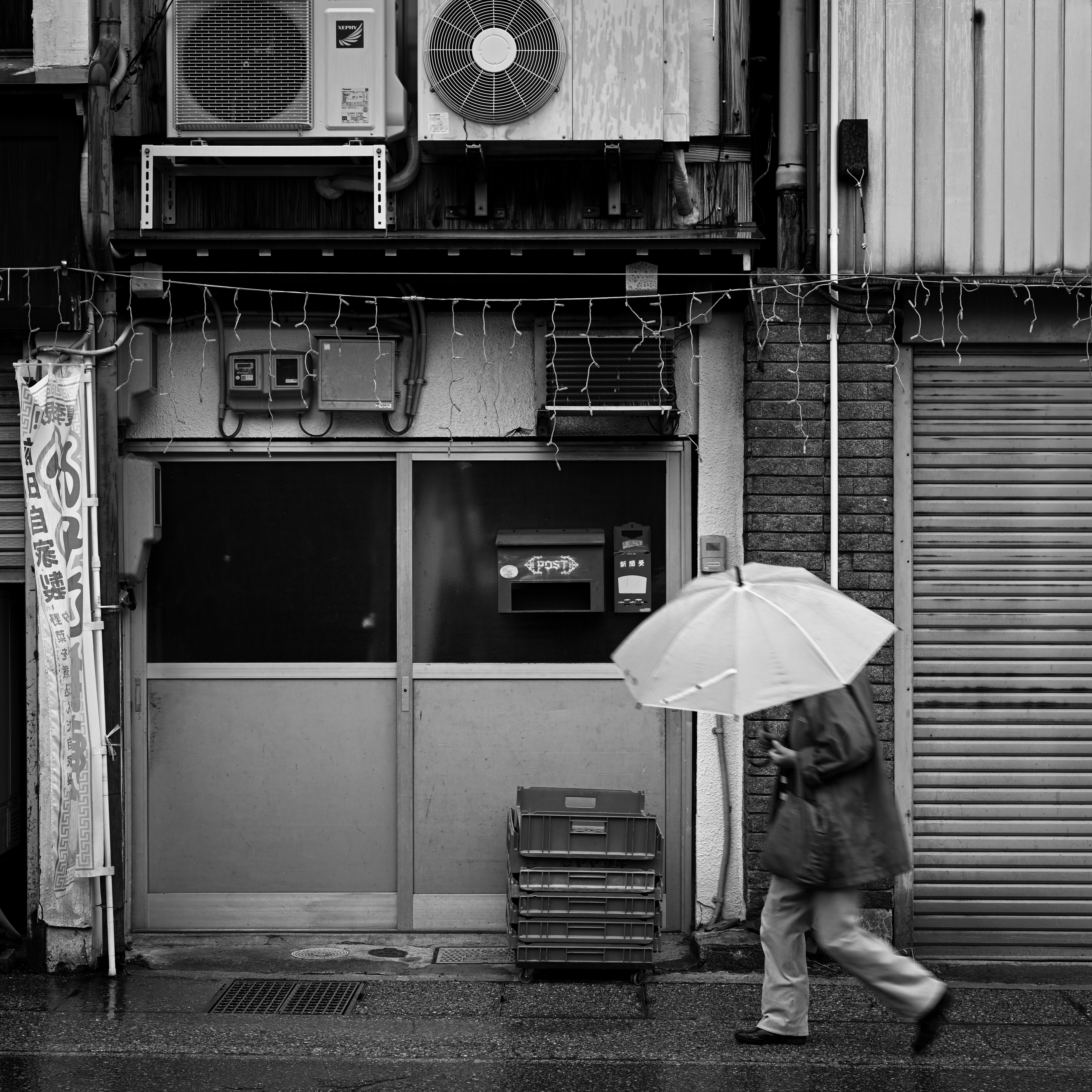雨の商店街で傘をさす歩行者のある路地の軒先