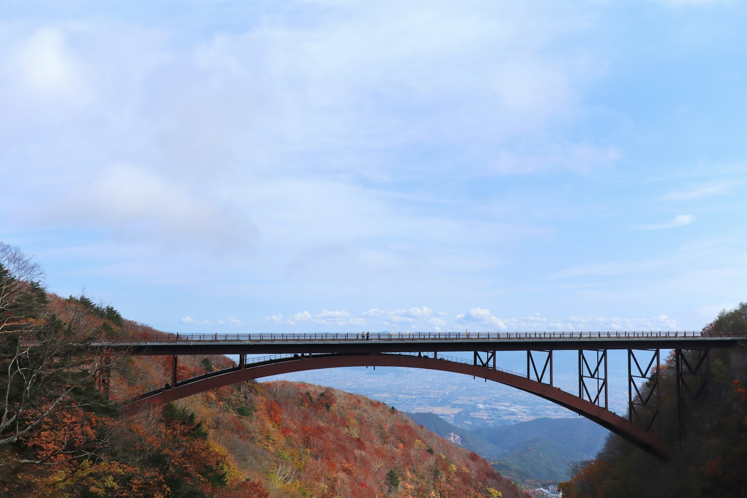 A scenic railway bridge spanning a colorful autumn landscape under a blue sky