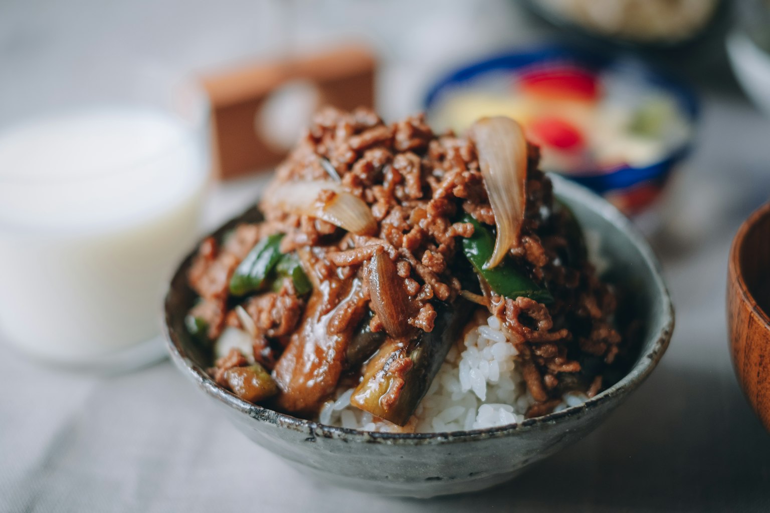 Un tazón de arroz cubierto con carne molida de res y verduras junto a una bebida