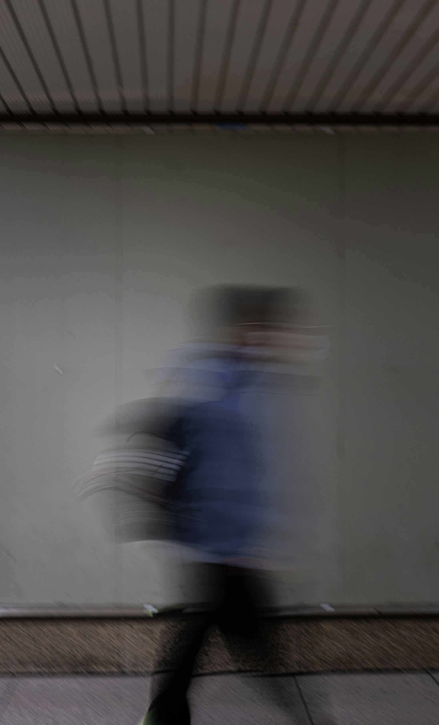 Figure floue marchant devant un mur vert portant une veste bleue