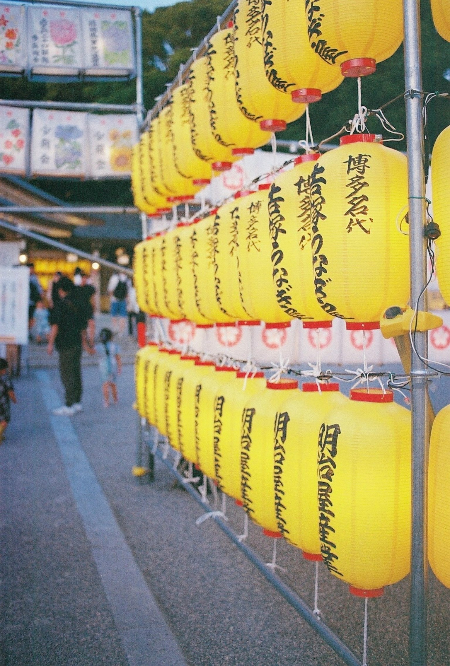 Une rangée de lanternes jaunes à un stand de festival avec des gens qui passent
