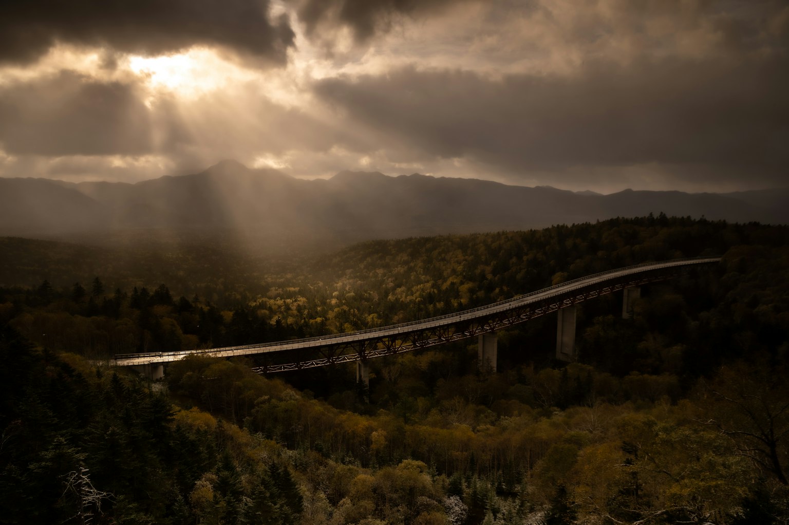 Un puente que se extiende entre montañas brumosas con luz atravesando las nubes