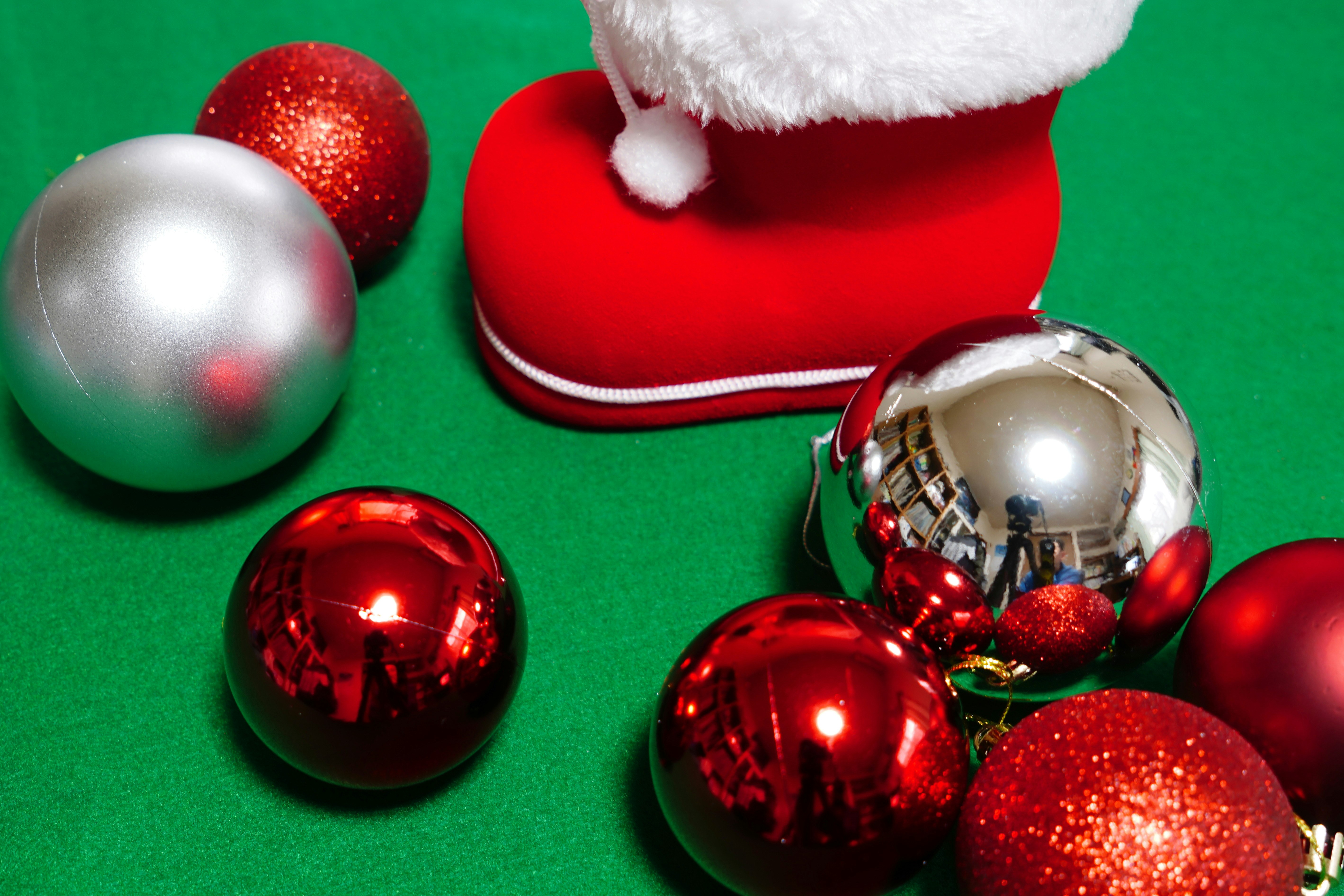 緑の布の上に並ぶクリスマスの装飾ボールとサンタ帽