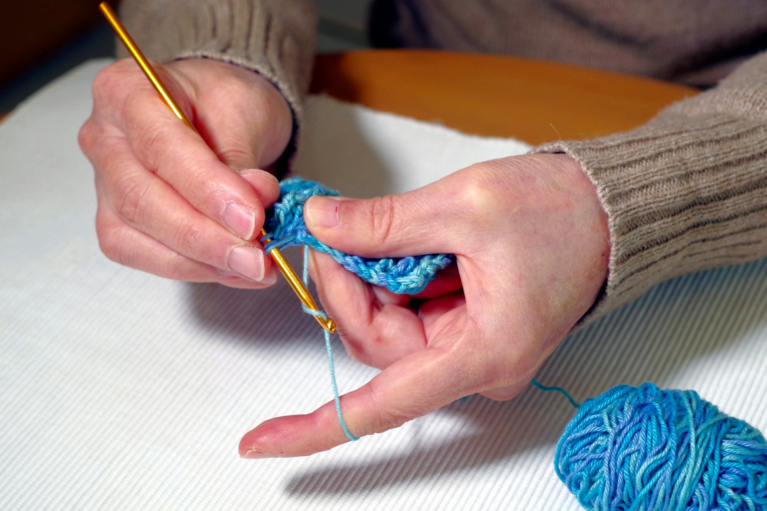 Hände, die mit blauer Wolle häkeln