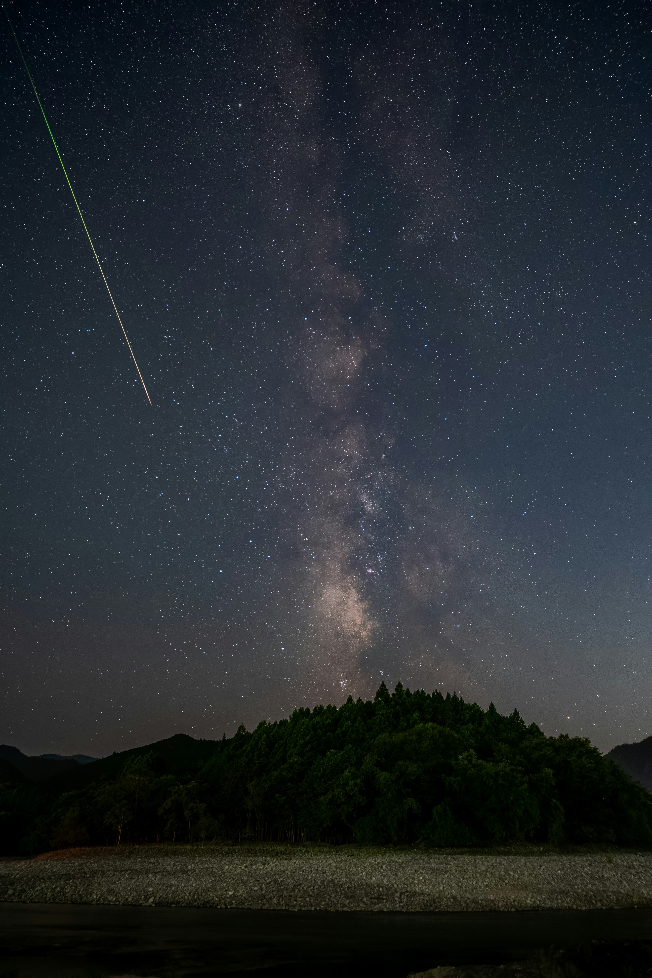 天の川と流れ星が夜空に広がる森の上の風景