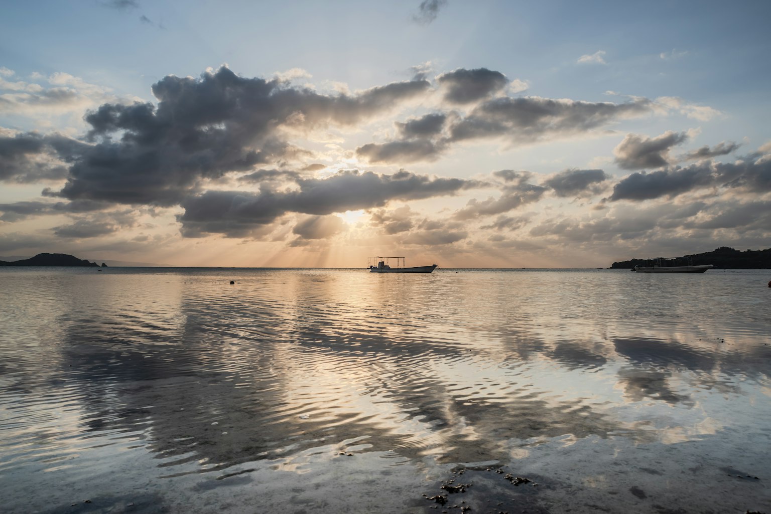 寧靜海面上，漁船在夕陽和雲彩的倒影中