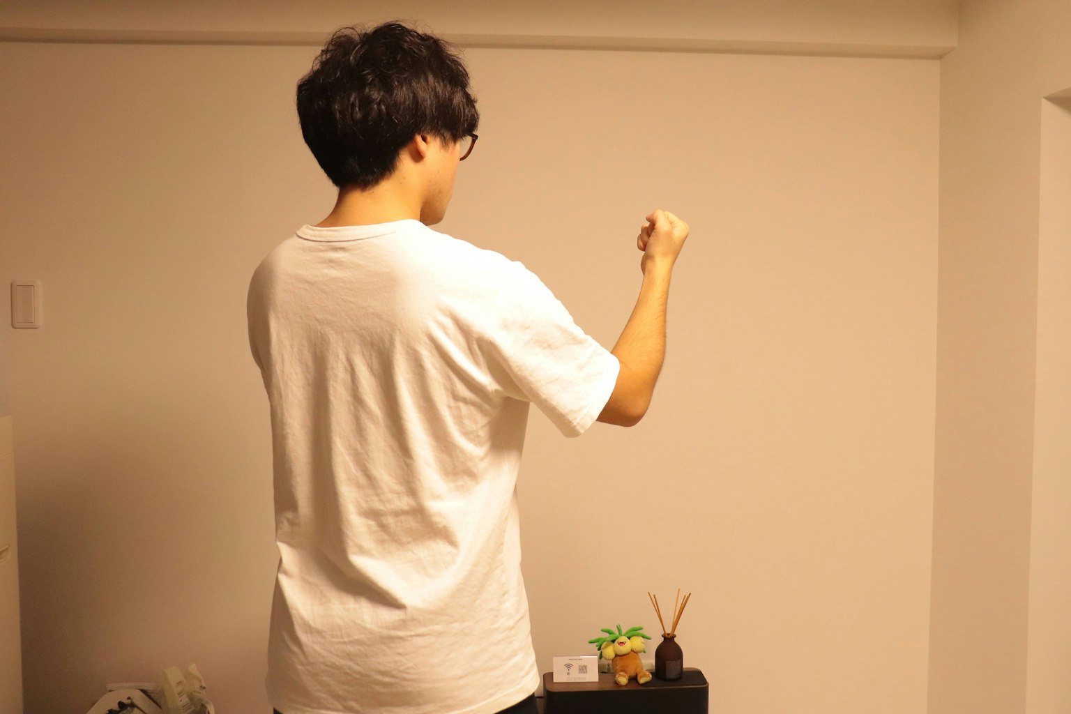 Một người đàn ông trong áo phông trắng đang ra hiệu về phía tường