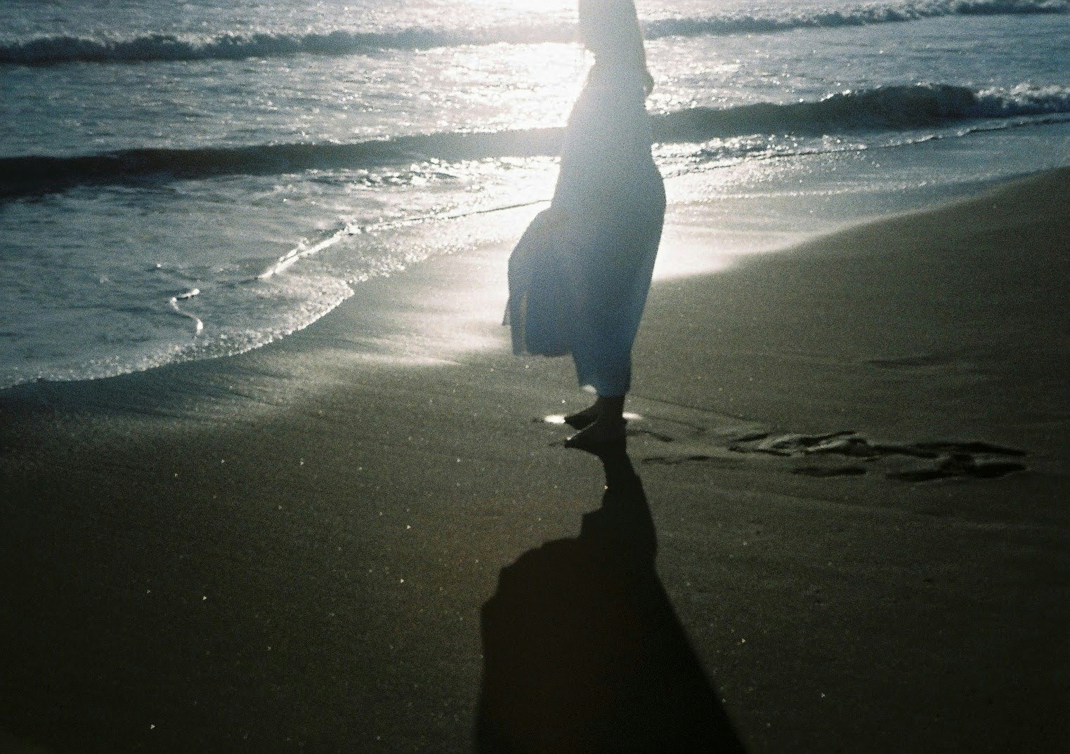 夕日に照らされた海辺を歩く人影