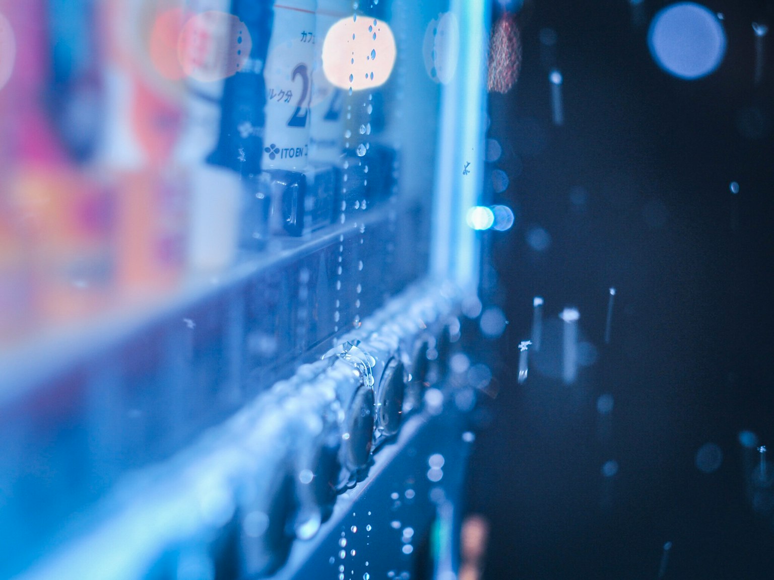 Cận cảnh máy bán hàng tự động được chiếu sáng bằng màu xanh với giọt nước trên kính và nền mờ