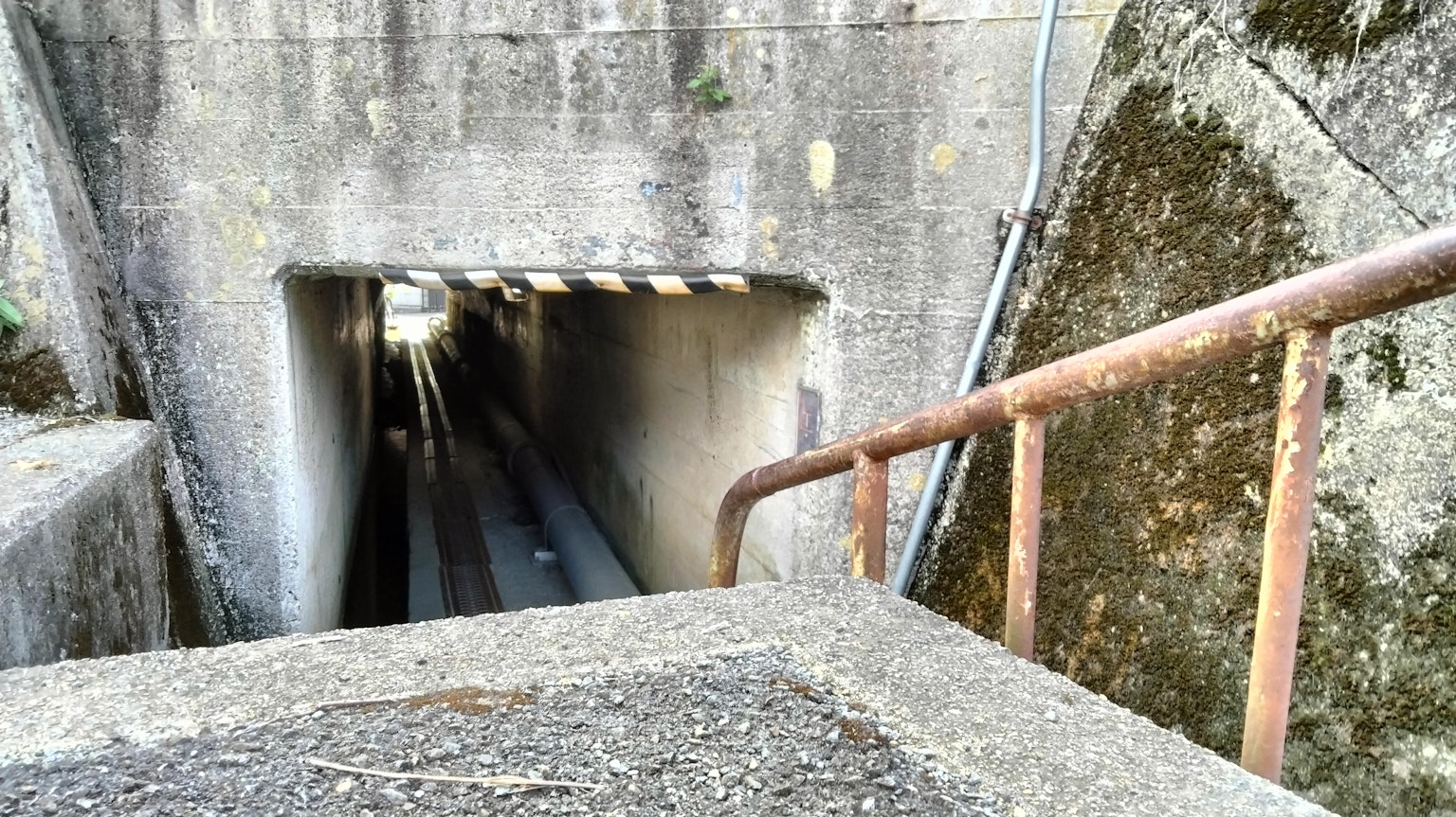 Immagine di un ingresso di tunnel in cemento con una ringhiera arrugginita