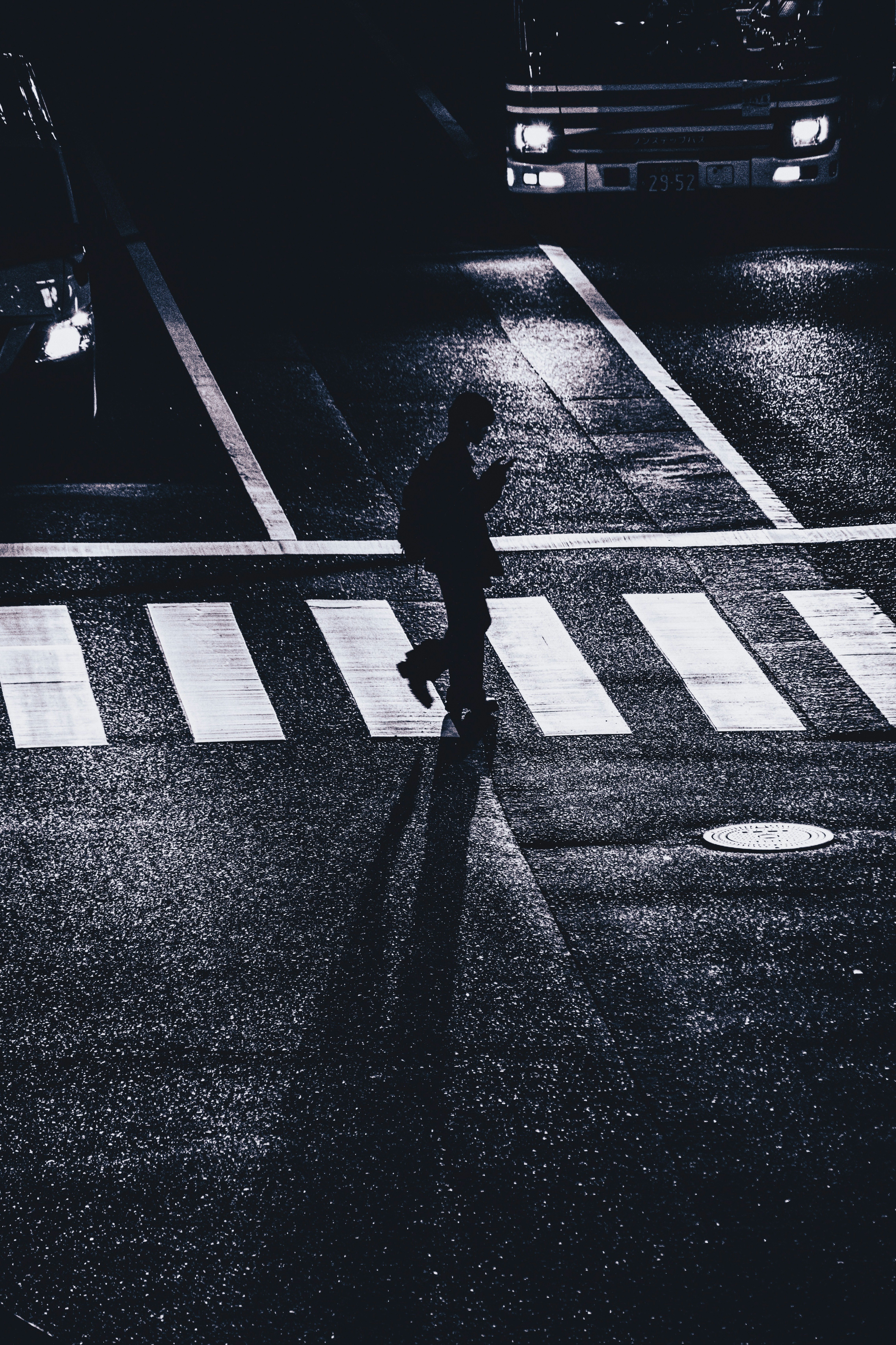 Silueta de una persona caminando por la noche en un paso de peatones con faros de vehículos
