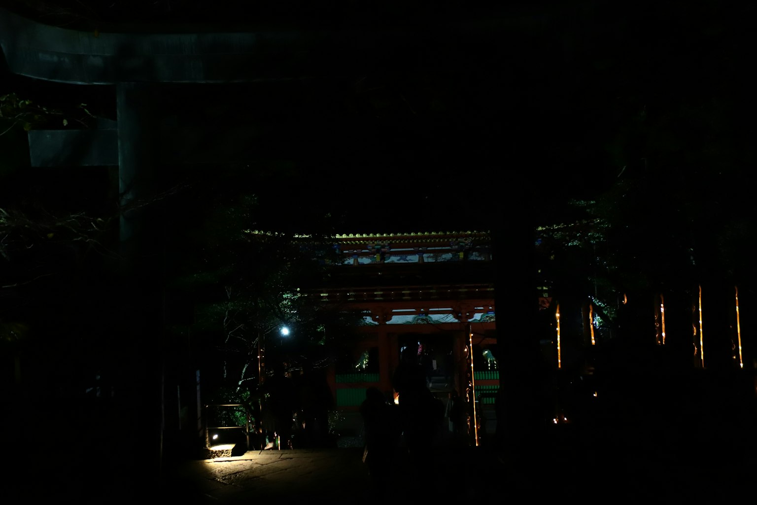 Pintu kuil yang diterangi di malam hari dengan siluet orang-orang