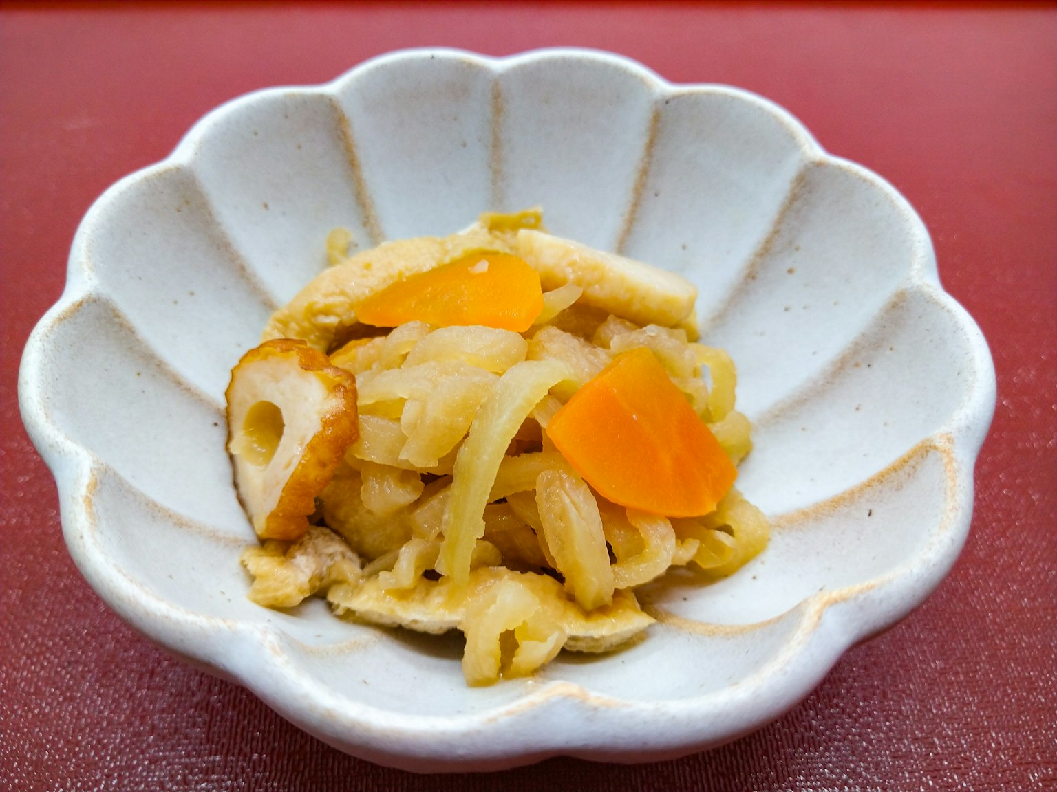Japanische Beilage in einer weißen, blütenblattförmigen Schüssel mit geschnittenem Fisch und Wurzelgemüse serviert