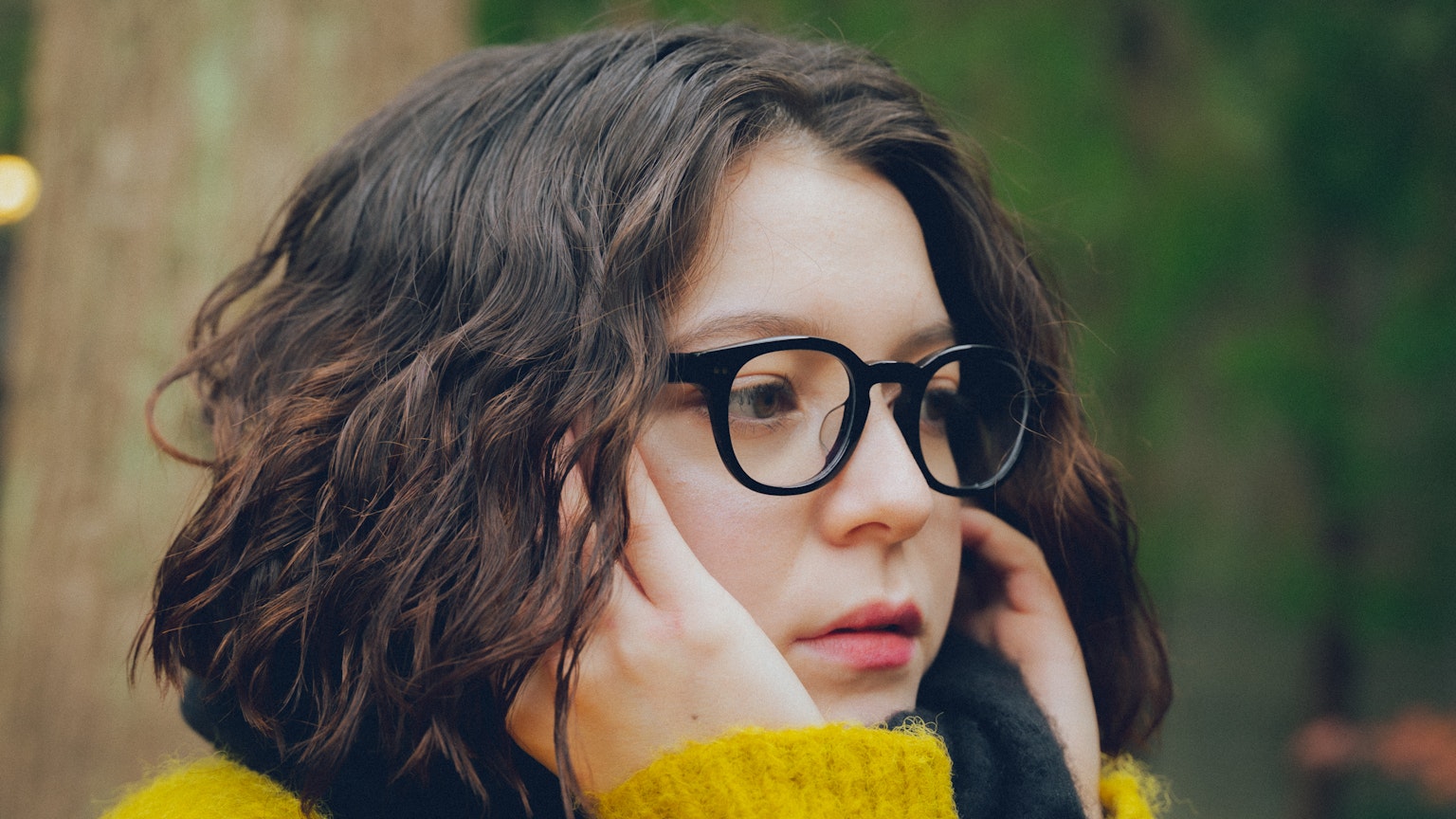 Giovane donna con capelli ricci che indossa occhiali toccando il viso all'aperto