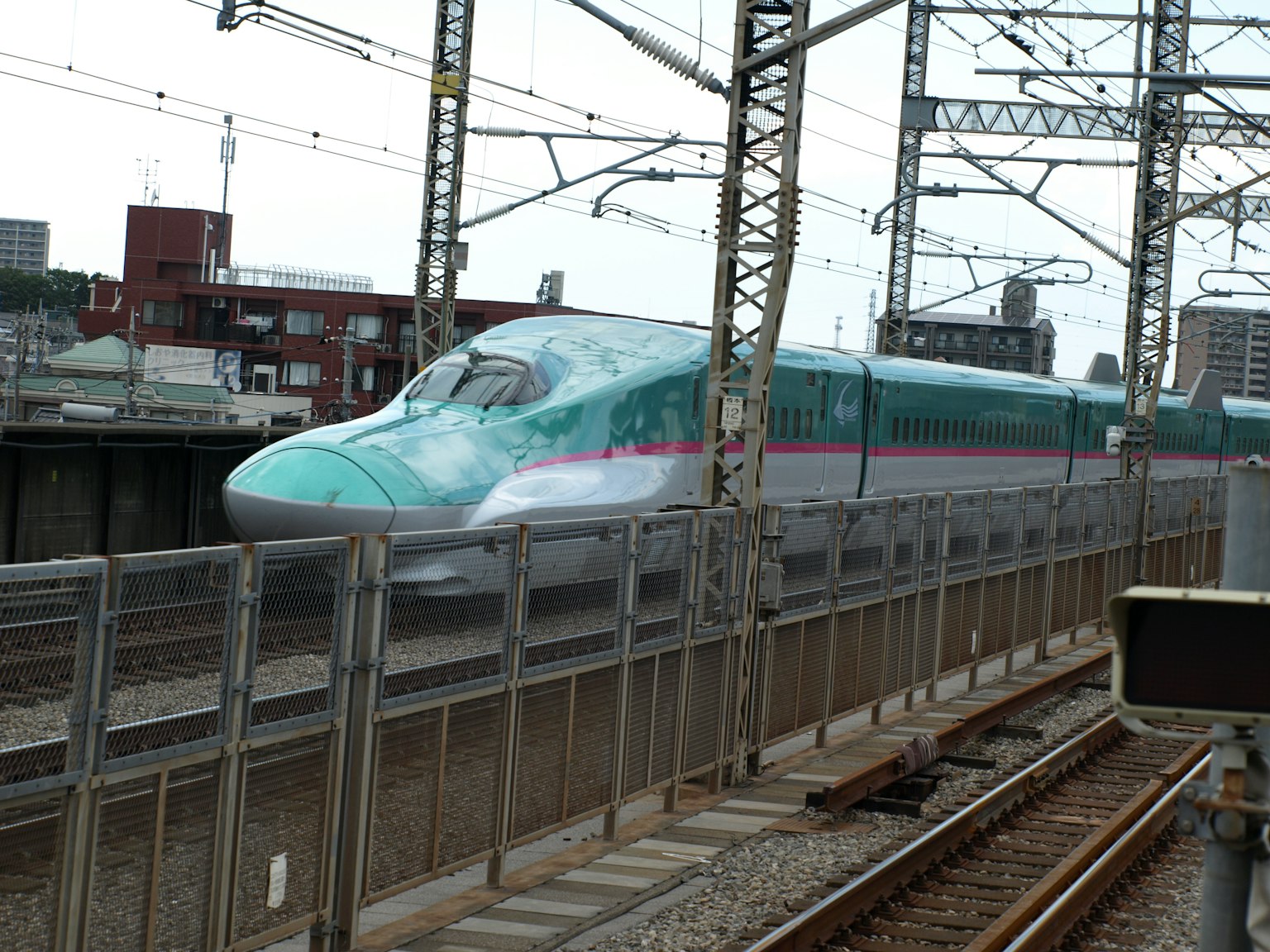 一列新幹線列車在車站快速經過，旁邊有建築物