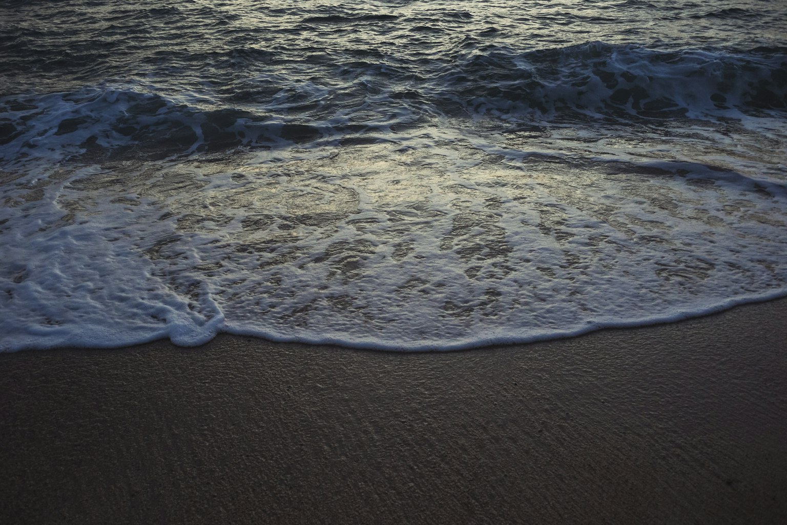Onde che si infrangono sulla spiaggia di sabbia al crepuscolo