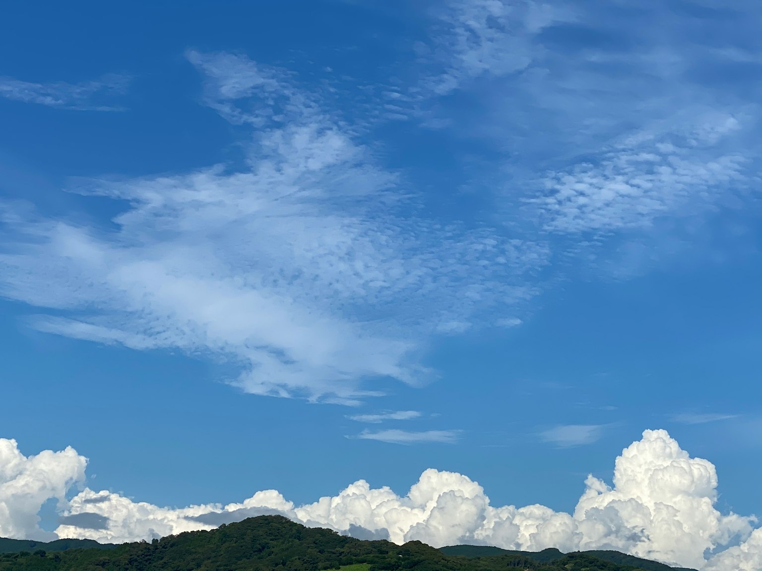 A clear blue sky with fluffy white clouds and a silhouette of a mountain