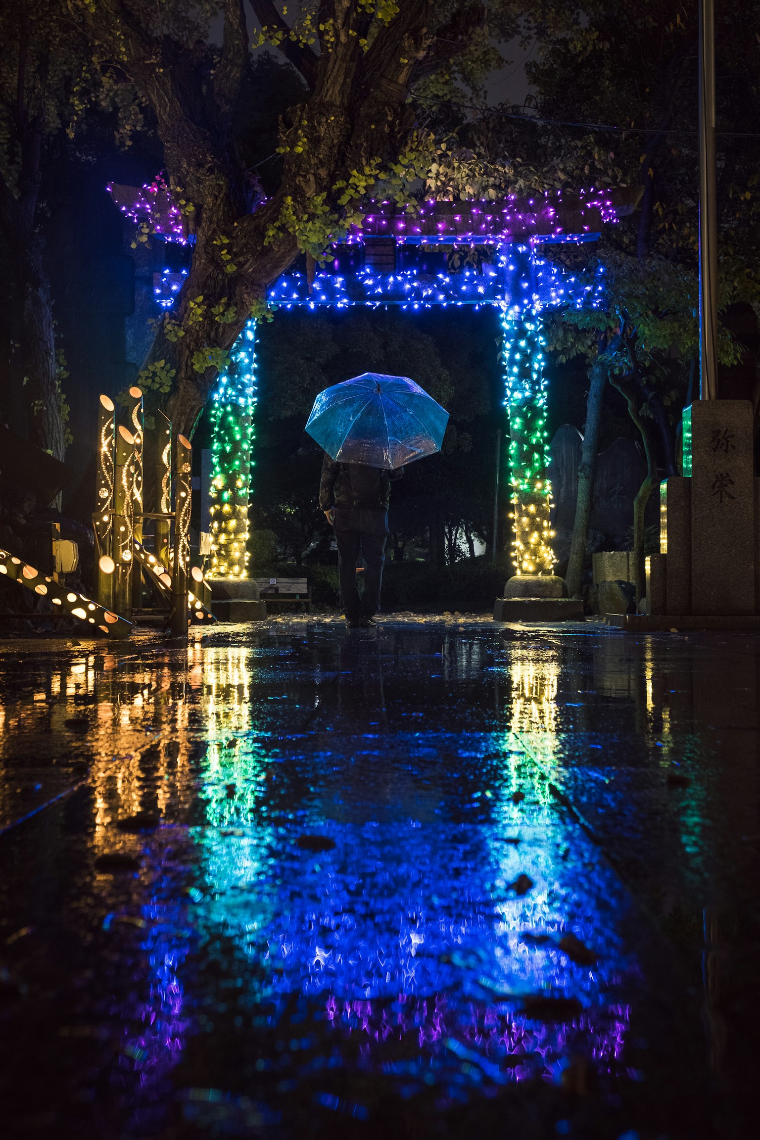 雨中反射的五彩灯装饰的拱门与撑伞的人