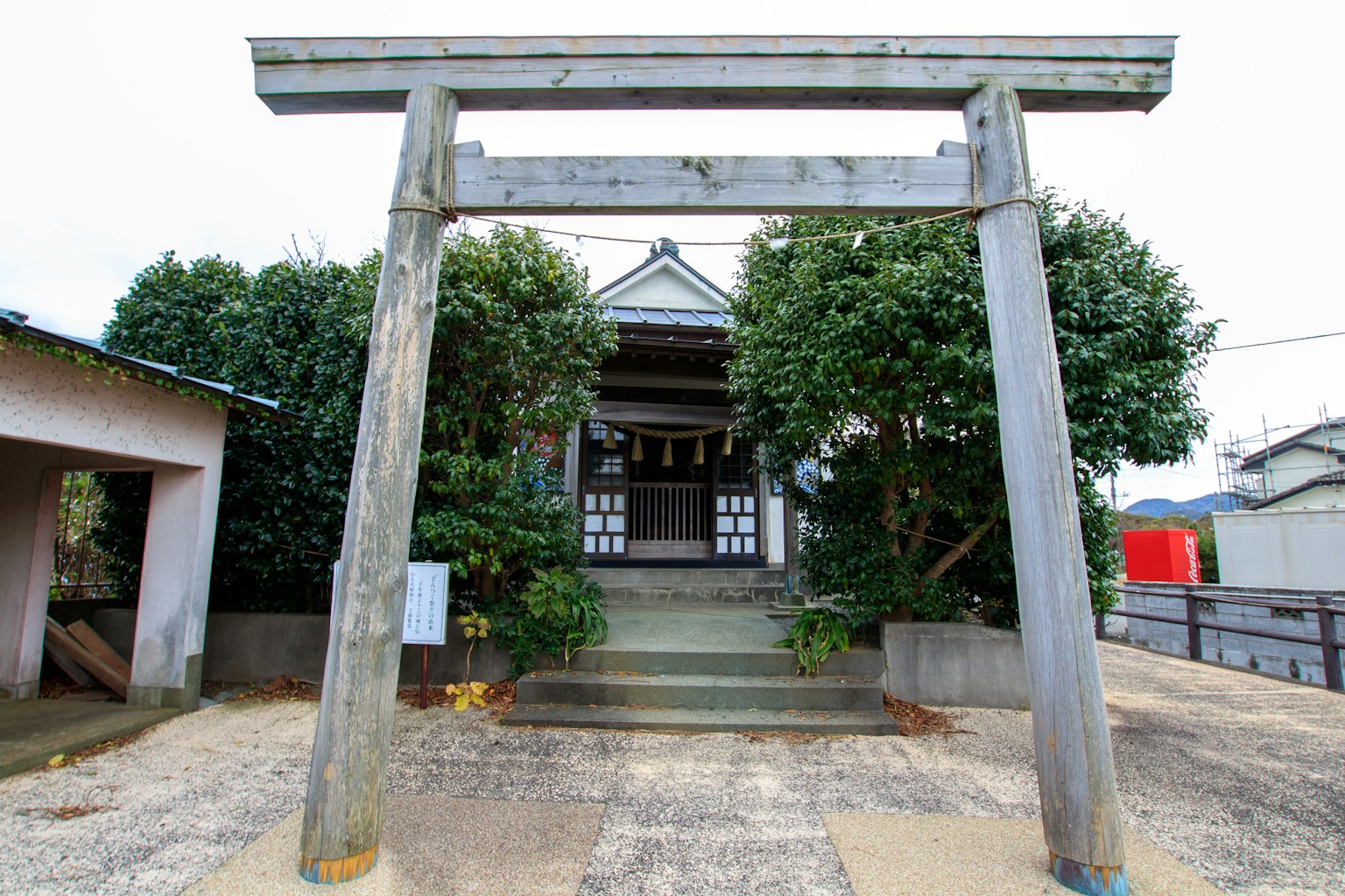 View of a shrine with a wooden torii gate surrounded by greenery and traditional architecture