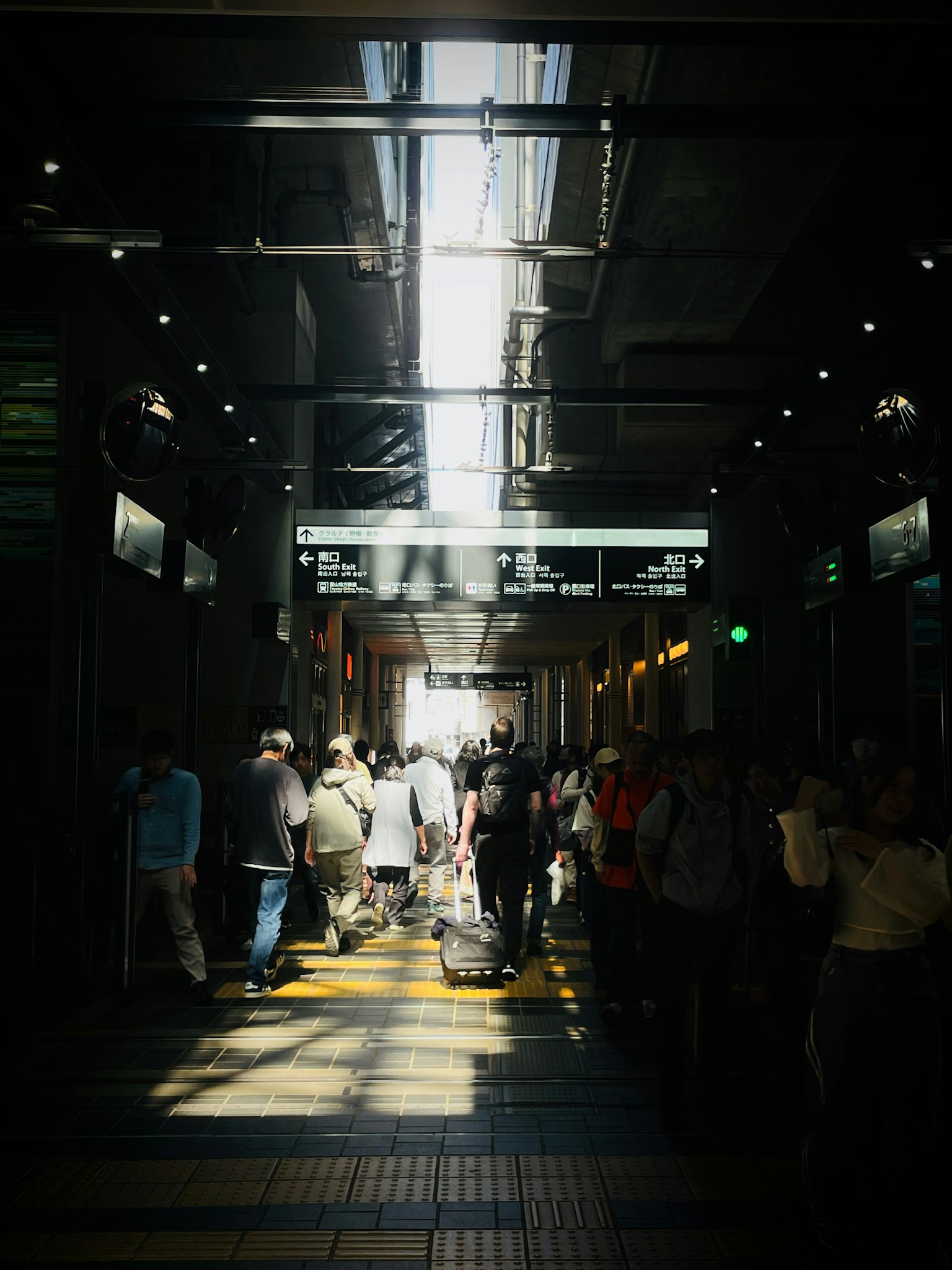Menschen gehen durch einen hellen Bahnhofskorridor mit Sonnenlicht, das hereinfällt