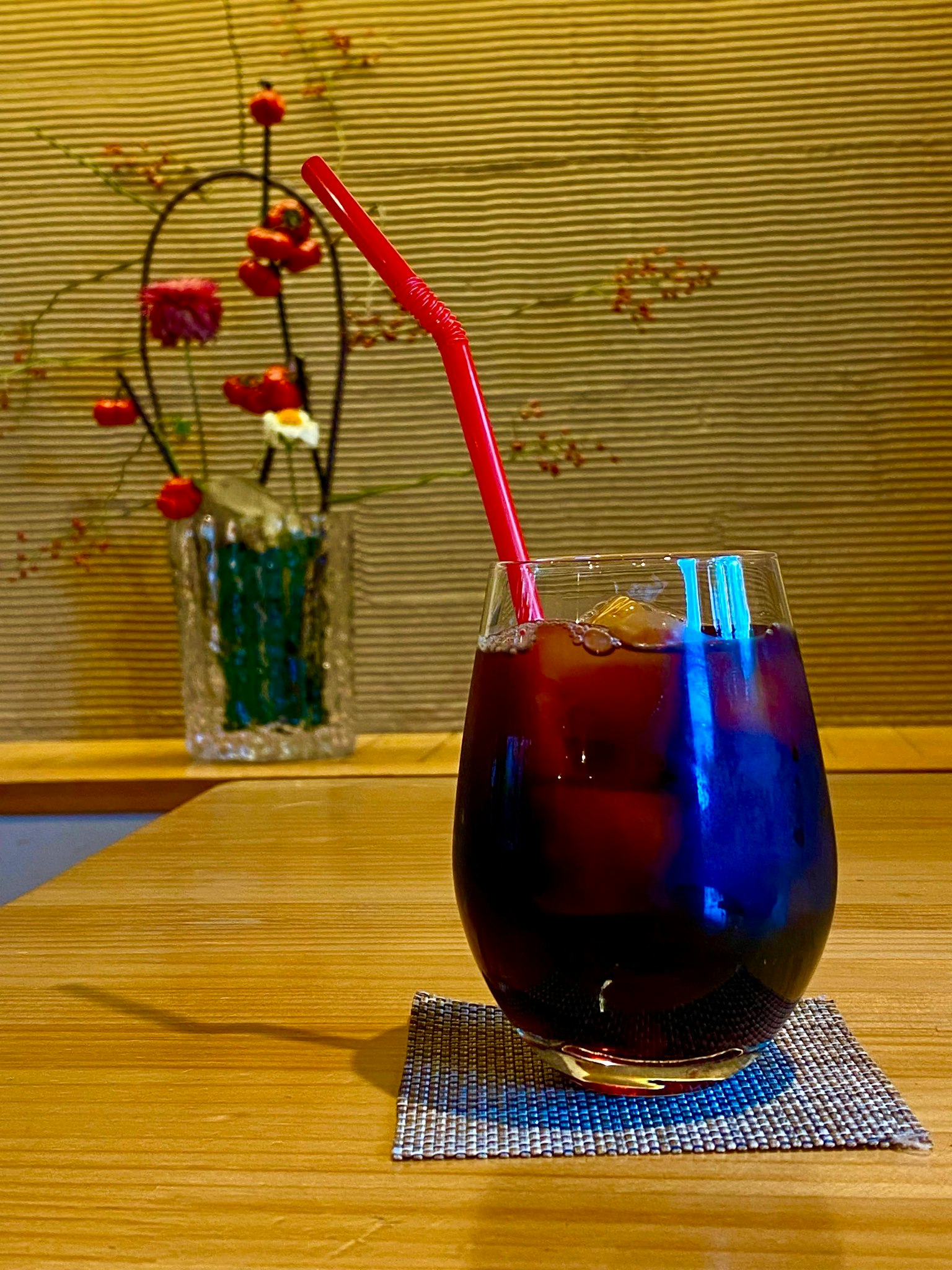 Un verre de boisson bleue avec une paille rouge sur une table en bois avec un arrangement floral en arrière-plan