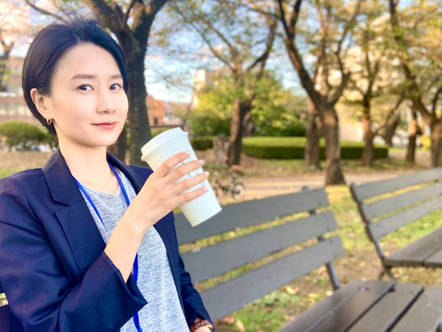 公园长椅上坐着的商务女性，手握咖啡杯