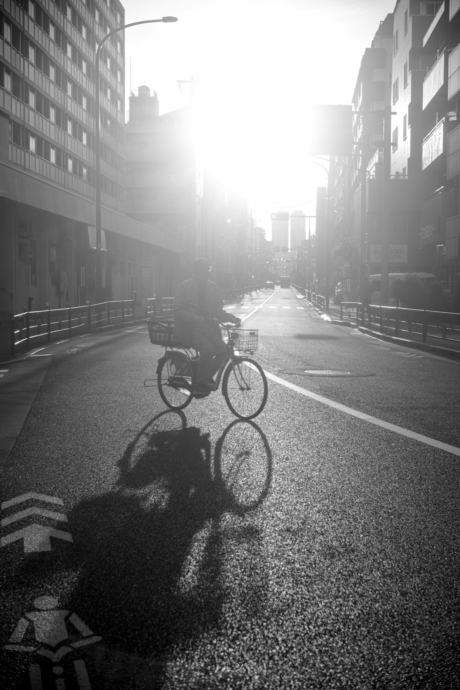 黑白照片中一個人在城市街道上騎自行車 背景中夕陽西下投射出長長的影子
