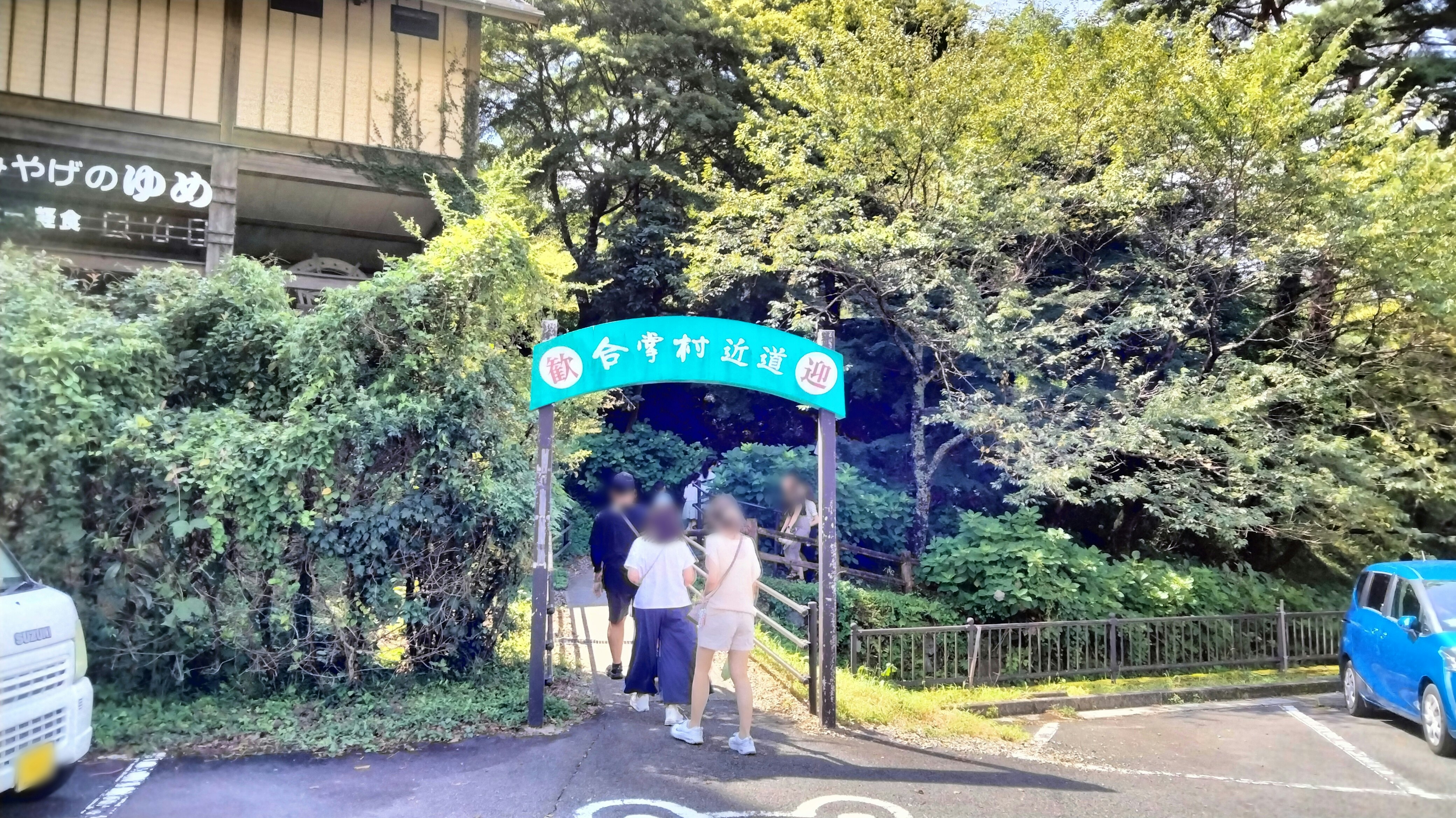 緑の並木道にある青い案内看板の前を歩く人々の入口
