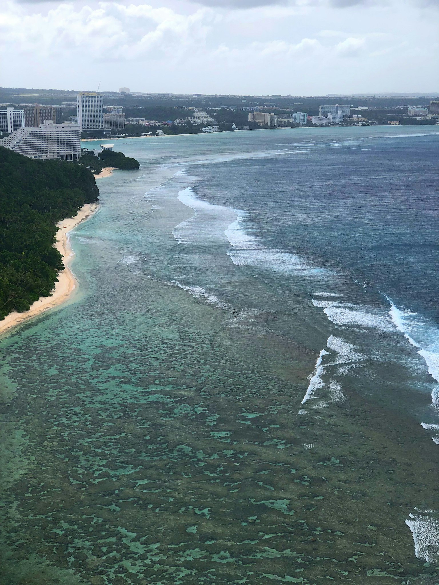 Pemandangan indah dengan laut biru, ombak putih, dan pulau hijau
