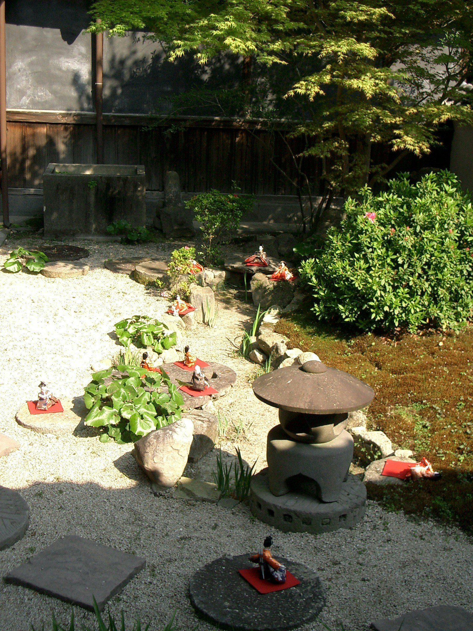 Japanese garden scene with stone path green plants lantern and red figurines arranged