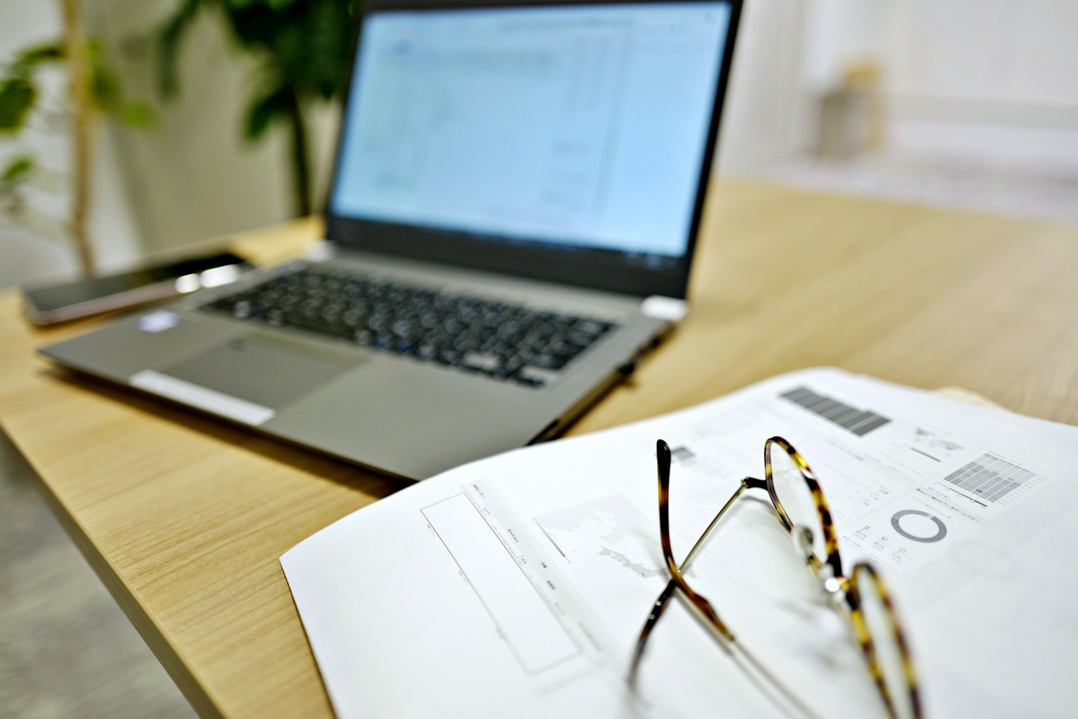 Ein Laptop auf einem Holztisch mit Brille und Dokumenten