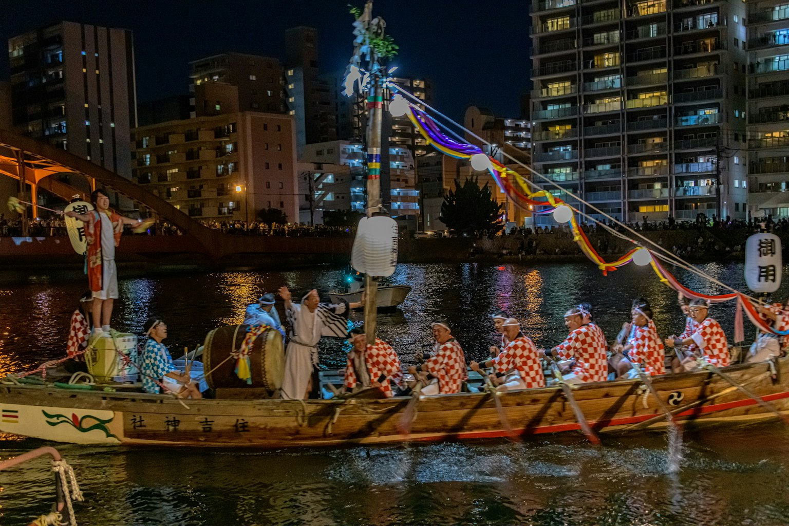 Des personnes en tenue traditionnelle sur un bateau festif naviguant le long de la rivière la nuit