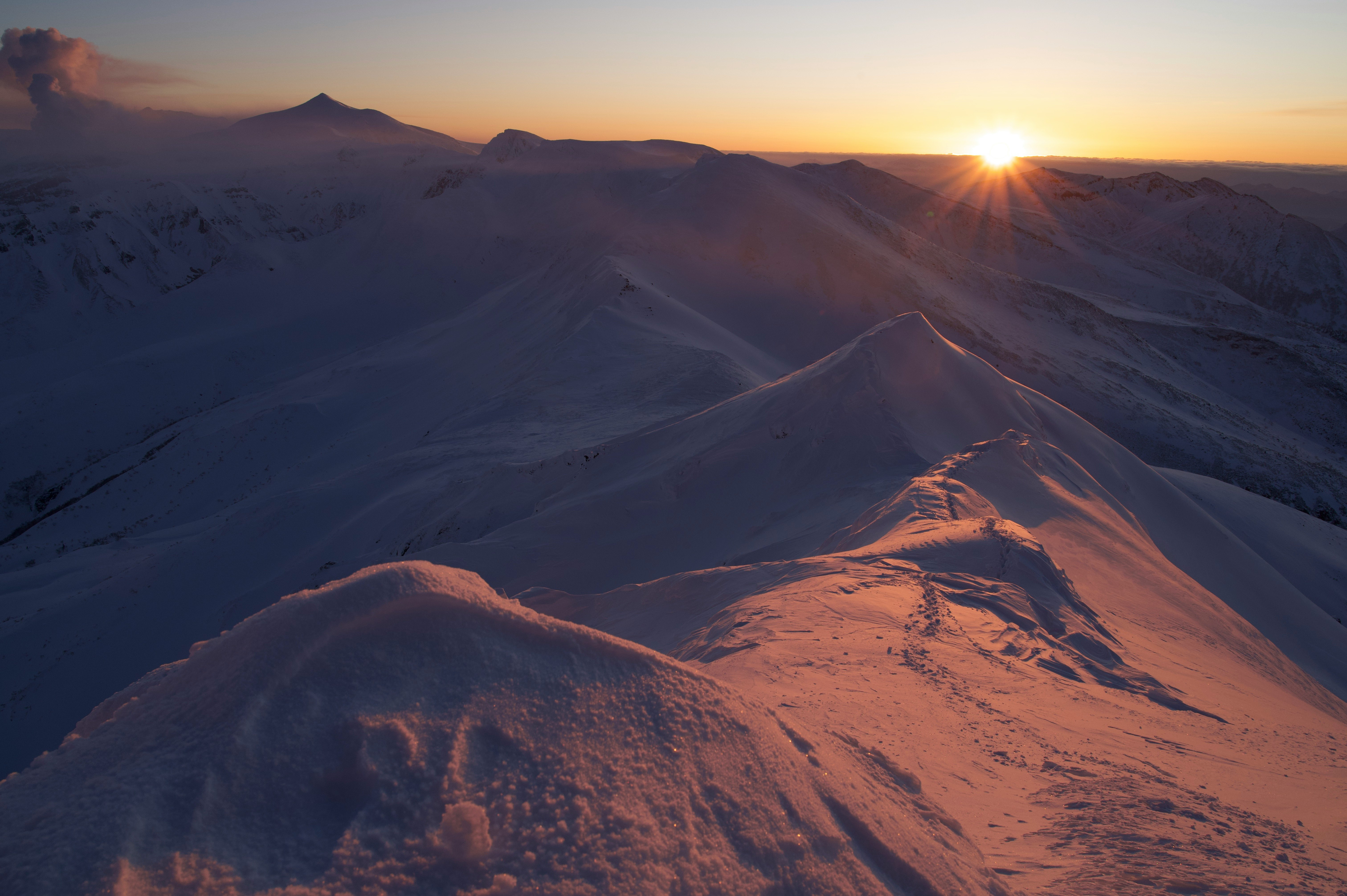 夕日に照らされた雪山の稜線と山道のパノラマ