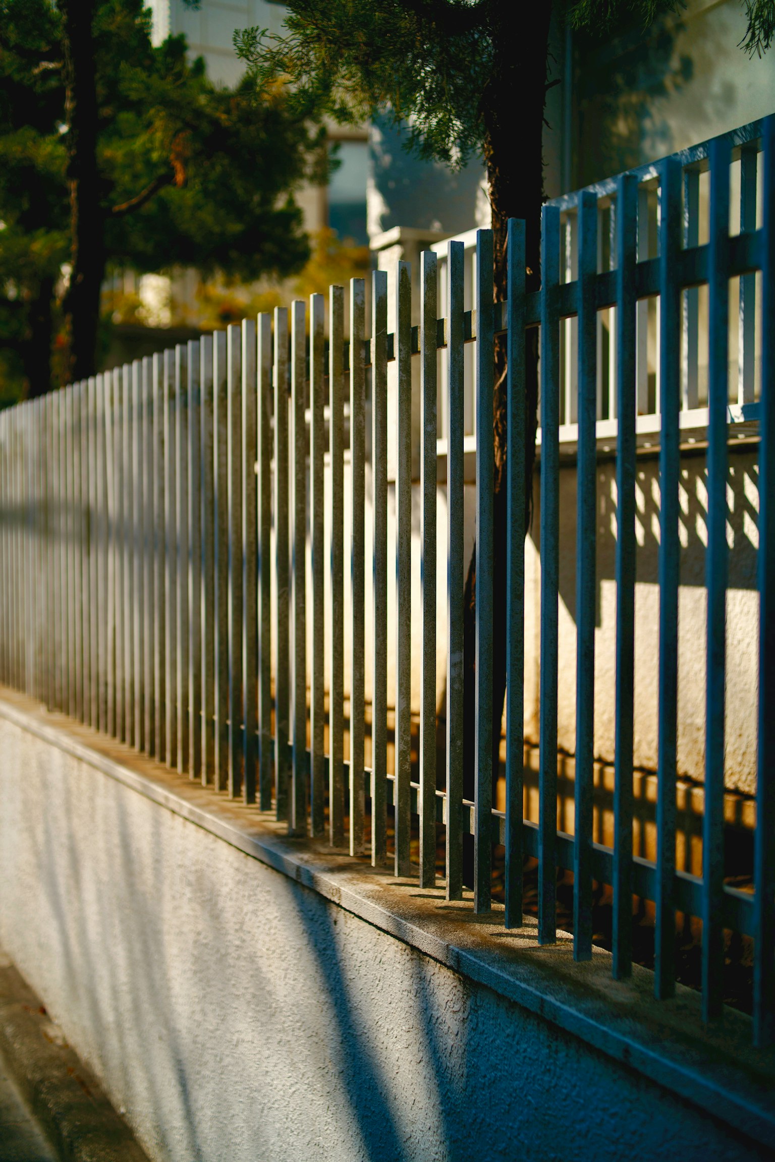 Metal fence standing along a street corner with shadows