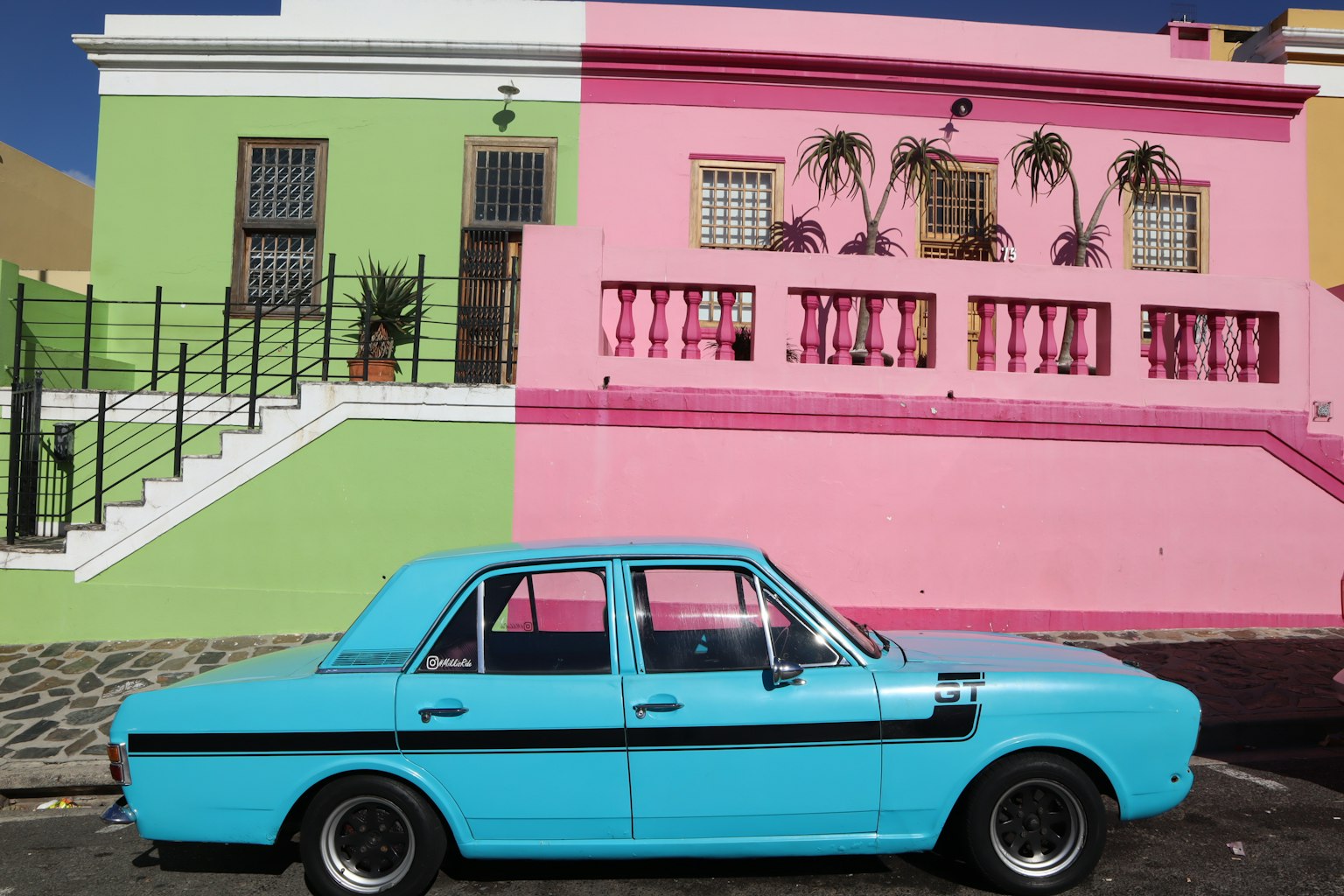 Ein leuchtend blauer Wagen vor bunten rosa und grünen Gebäuden