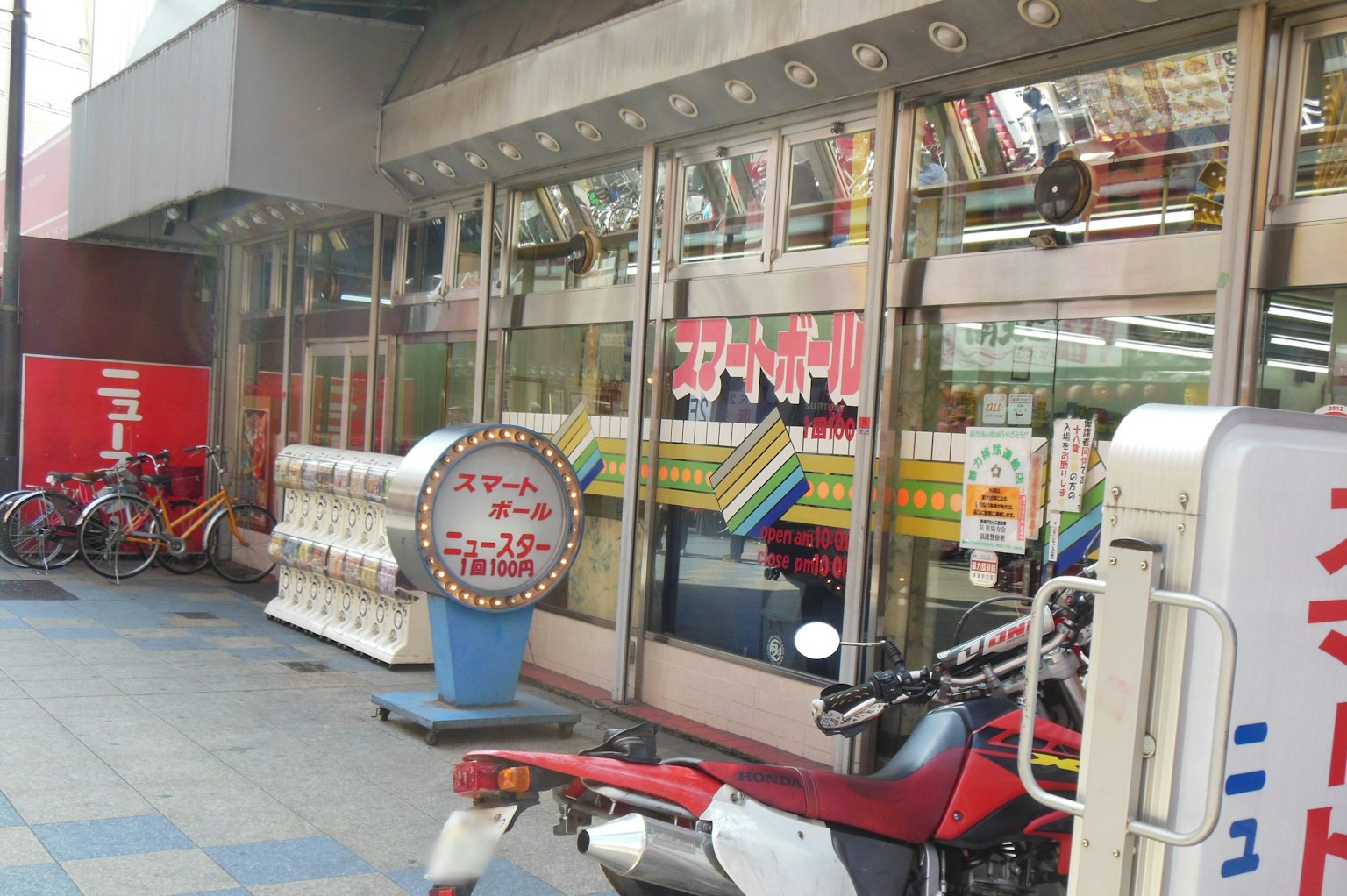 Außenansicht eines Geschäfts mit geparkten Fahrrädern und einem Motorrad Bunte Schilder und Glaseingang