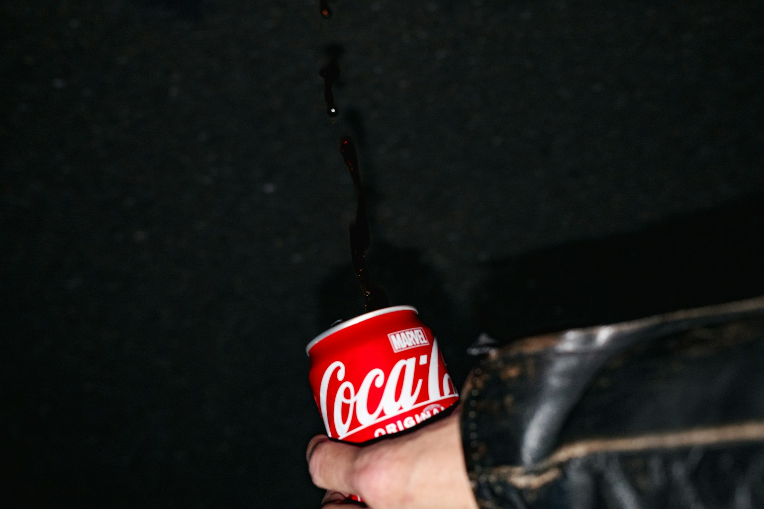 Một bàn tay cầm một lon Coca-Cola đỏ với chất lỏng đang tràn ra