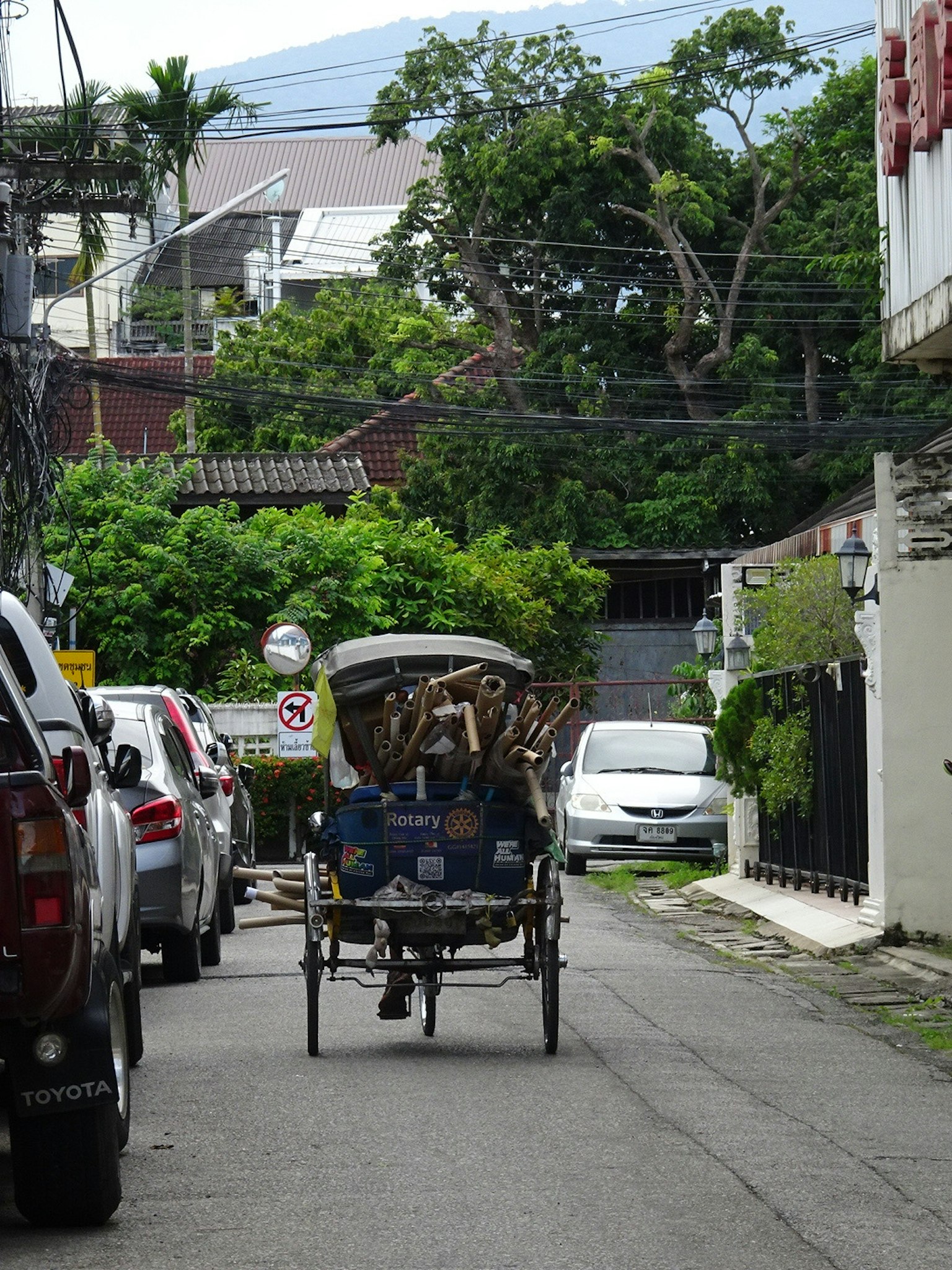 Un taxi tricycle dans une rue étroite entourée de voitures garées et de verdure