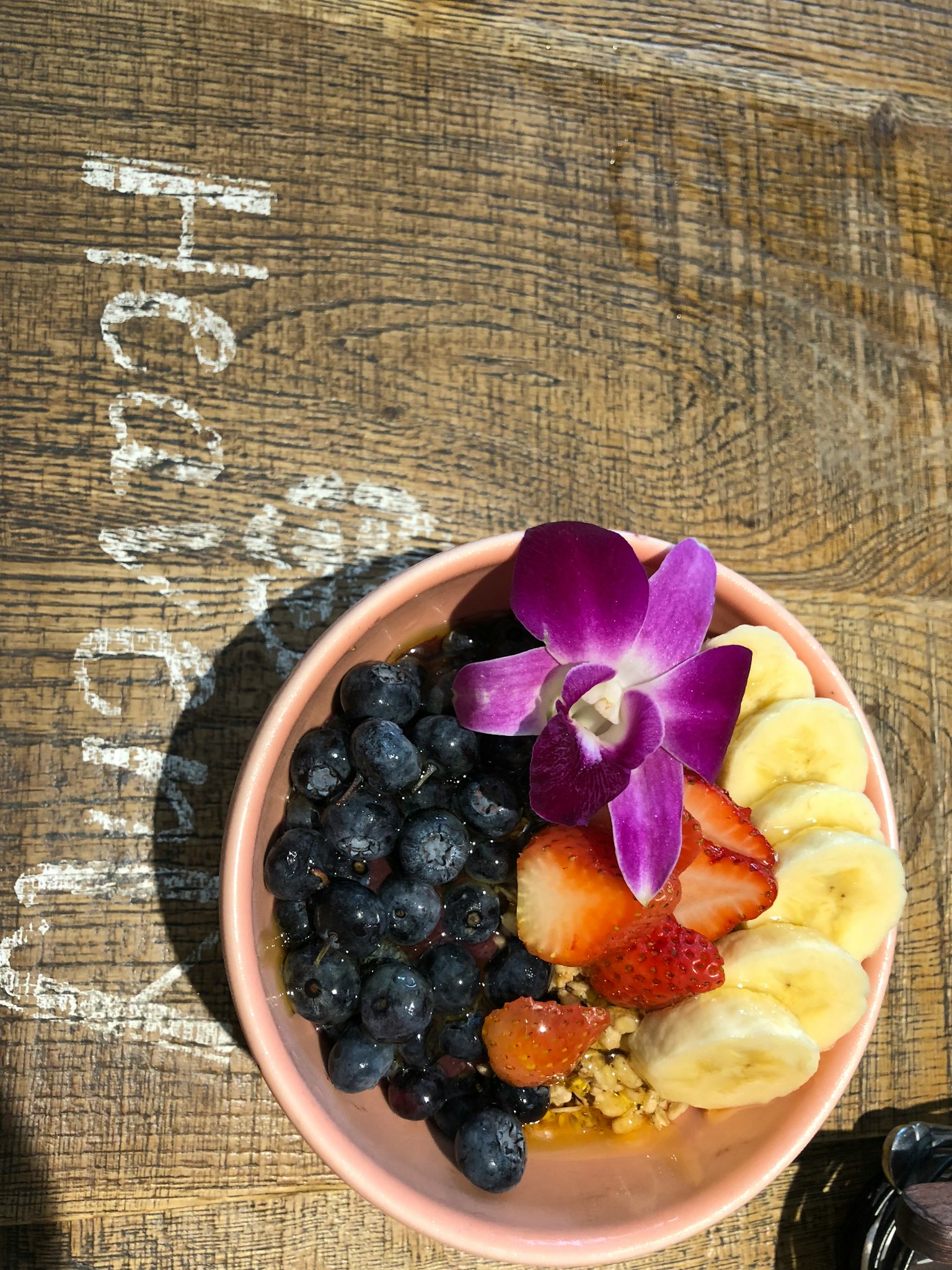 Mangkok penuh dengan buah berwarna-warni termasuk blueberry pisang dan stroberi dihiasi dengan bunga ungu