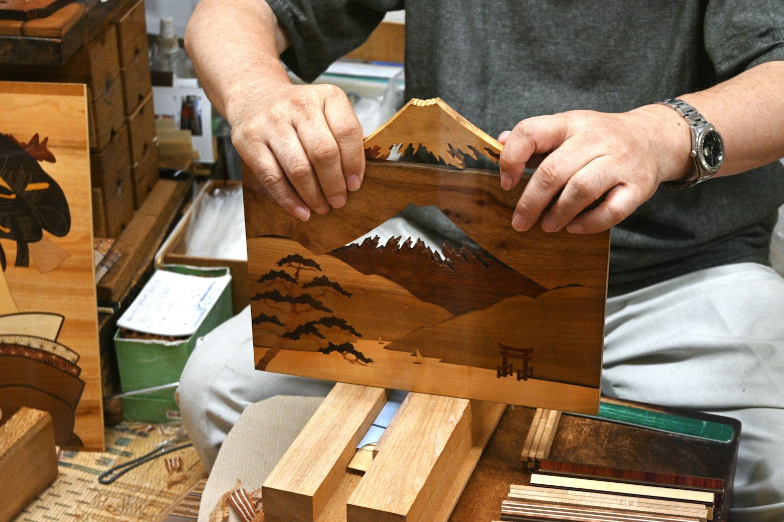 職人が山の風景を描いた木製のパネルを持っている