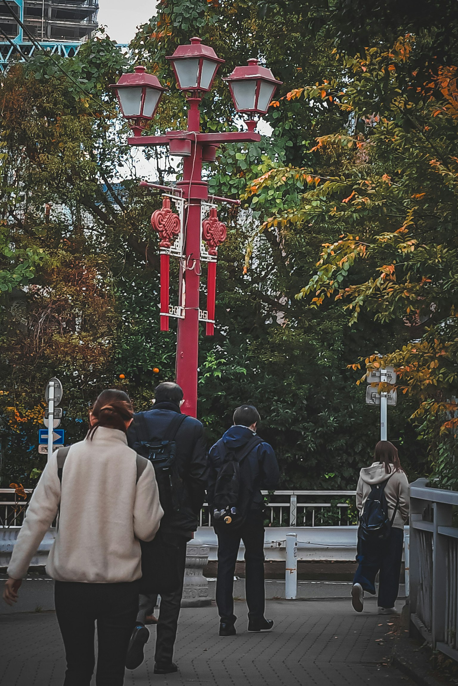 Personas caminando por un camino con farolas rojas y árboles de otoño