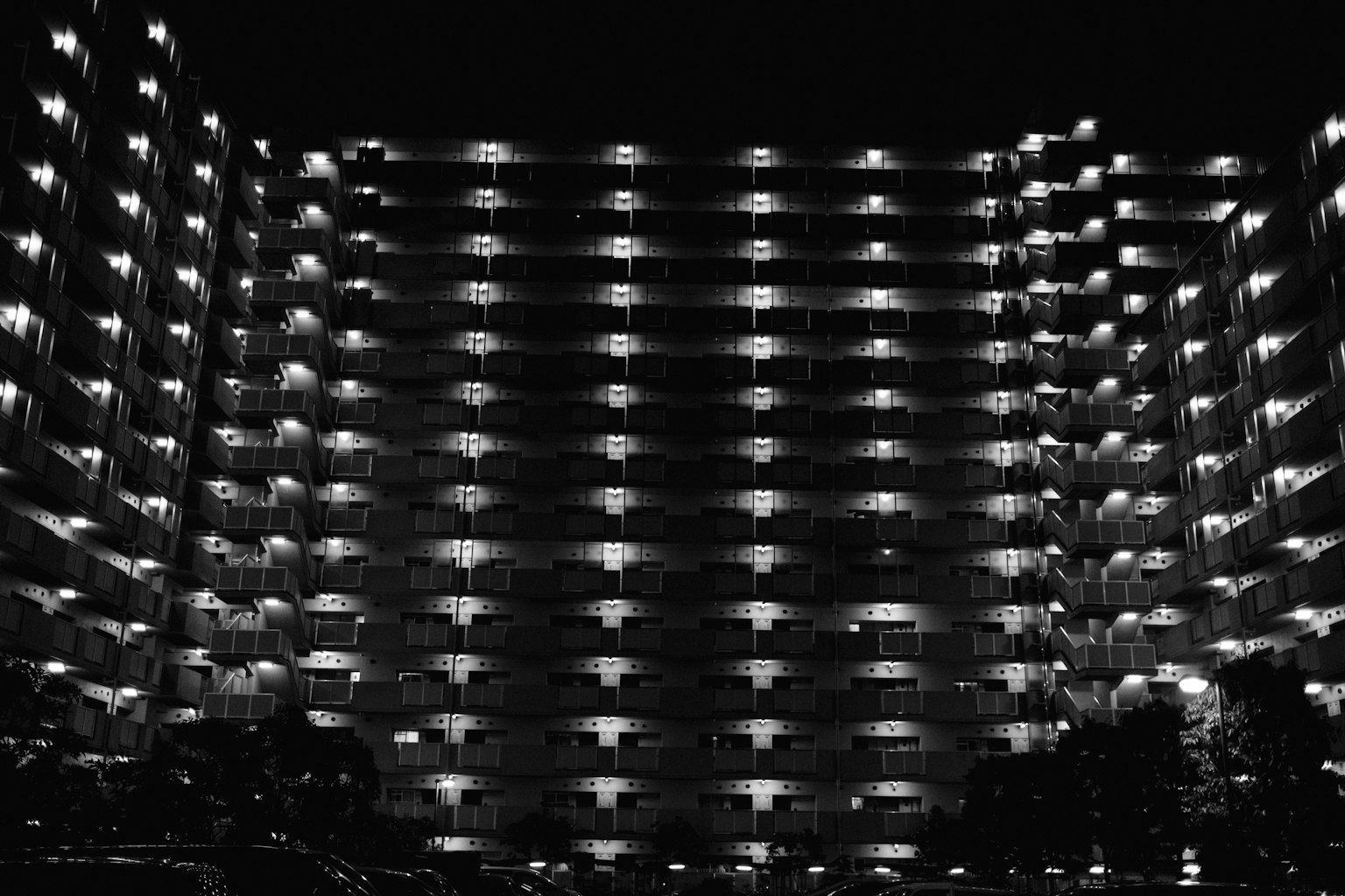 Fotografía en blanco y negro de un edificio de apartamentos por la noche con fachada iluminada destacada